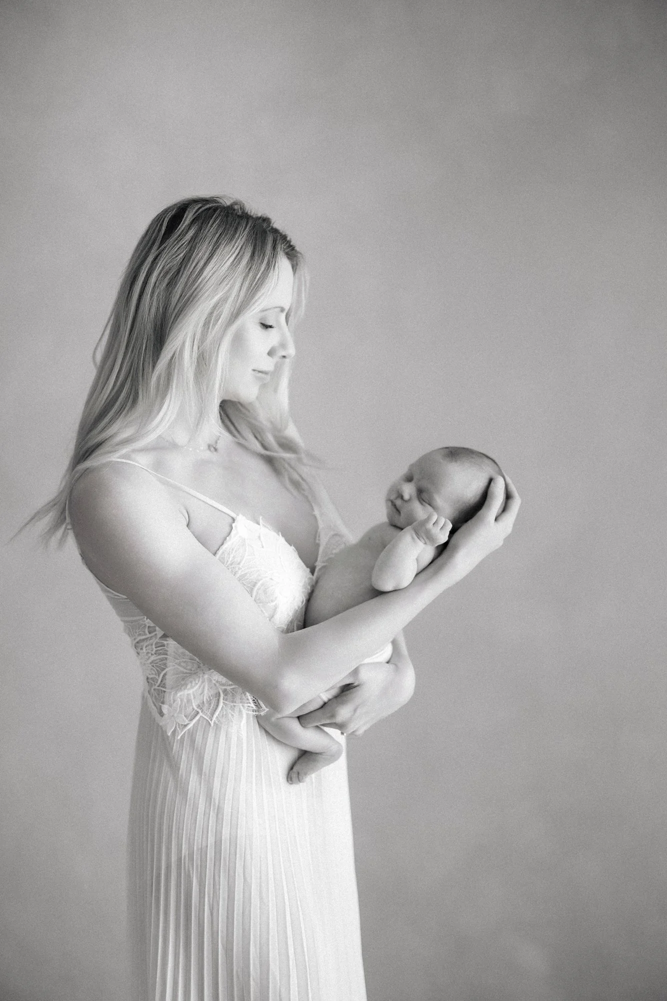 Black and white portrait of a mother looking lovingly at her newborn during a studio session.