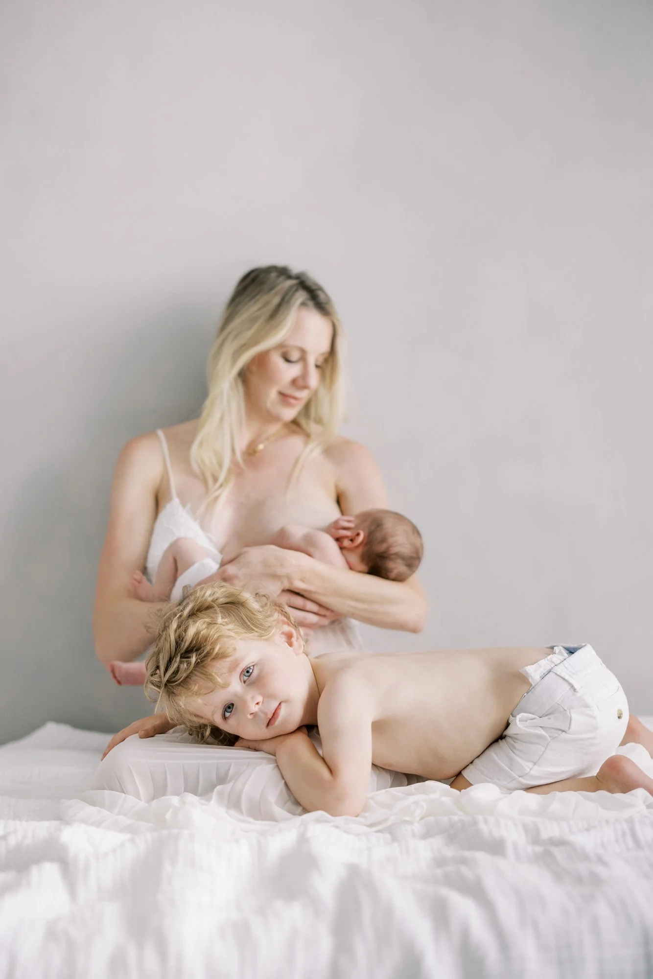 Mother cuddling her newborn while her toddler rests beside her during a cozy family newborn session.