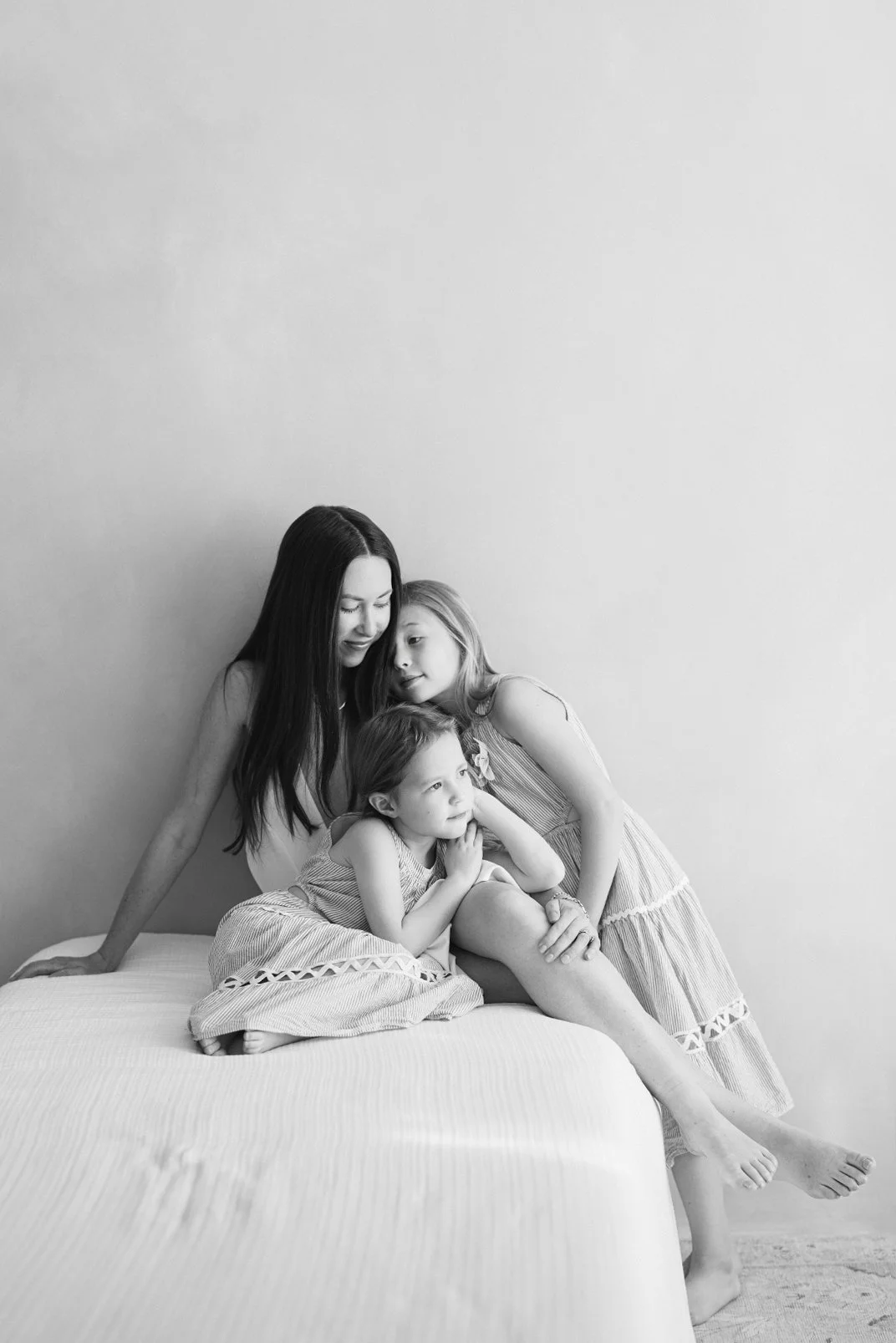 Black and white studio portrait of a mother snuggling with her children on a bed