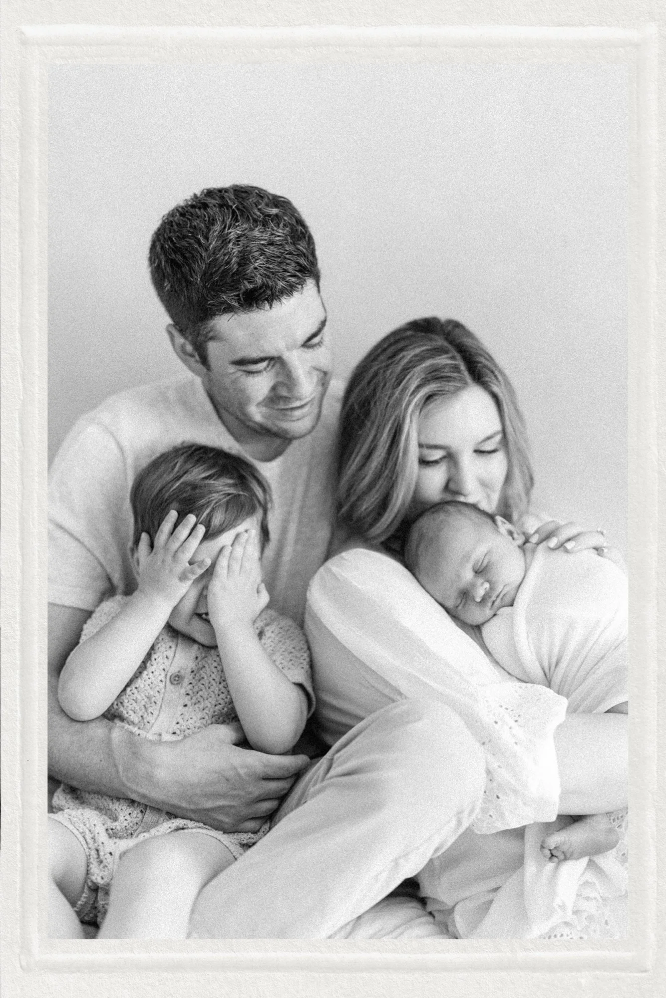 Matted photo of family and son playing peek-a-boo during newborn portrait
