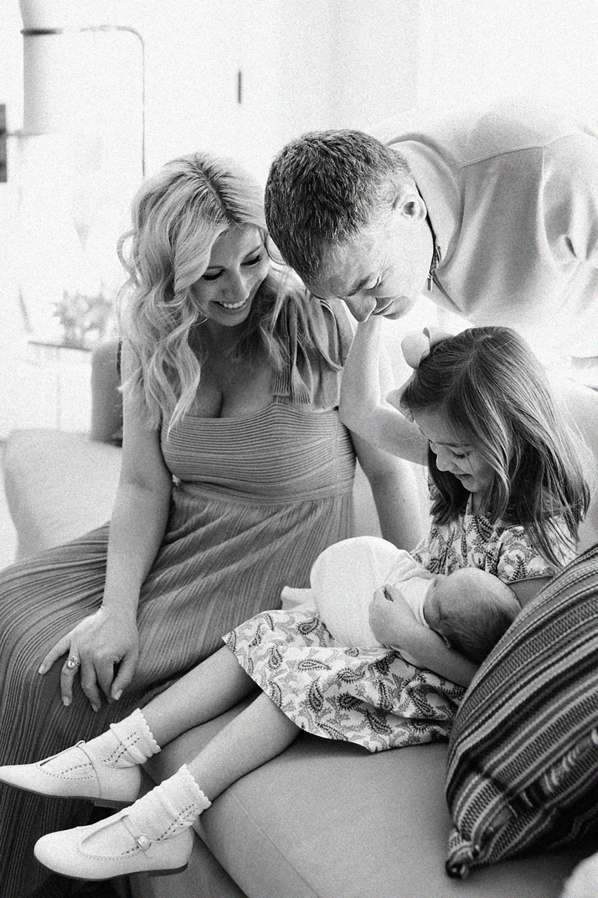 Black and white portrait of parents and older sibling gathered around their newborn during an in-home family session.