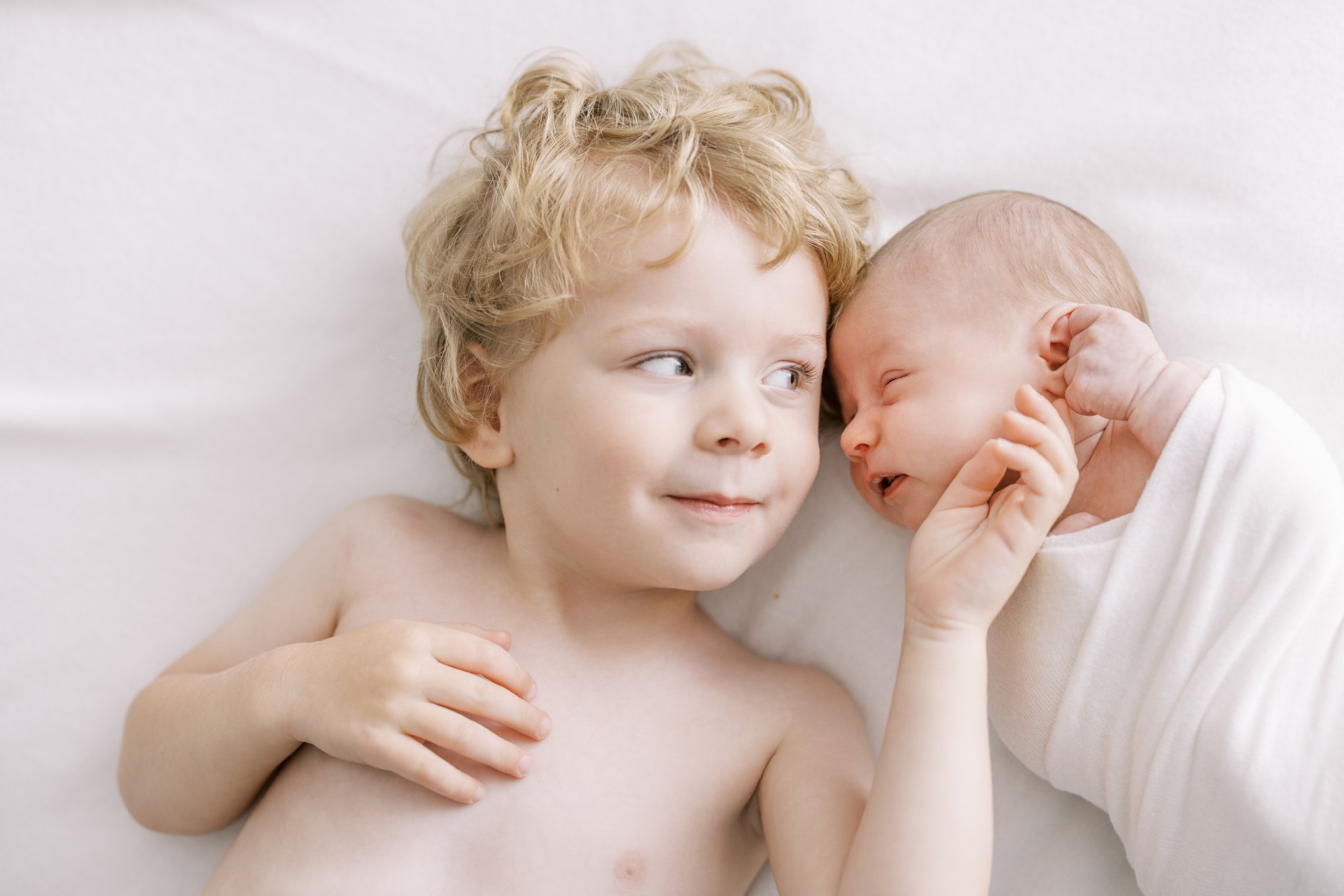 Older sibling cuddling beside a sleeping newborn during a relaxed family newborn photography session.