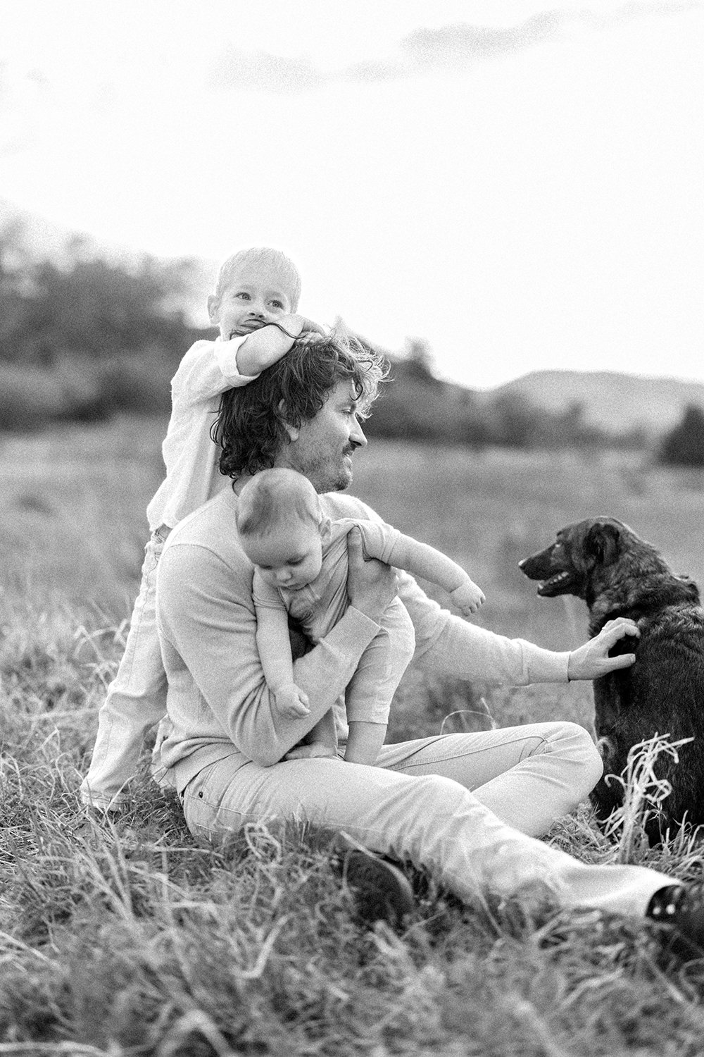 Black and white portrait of a father sitting in a field and playing with his children
