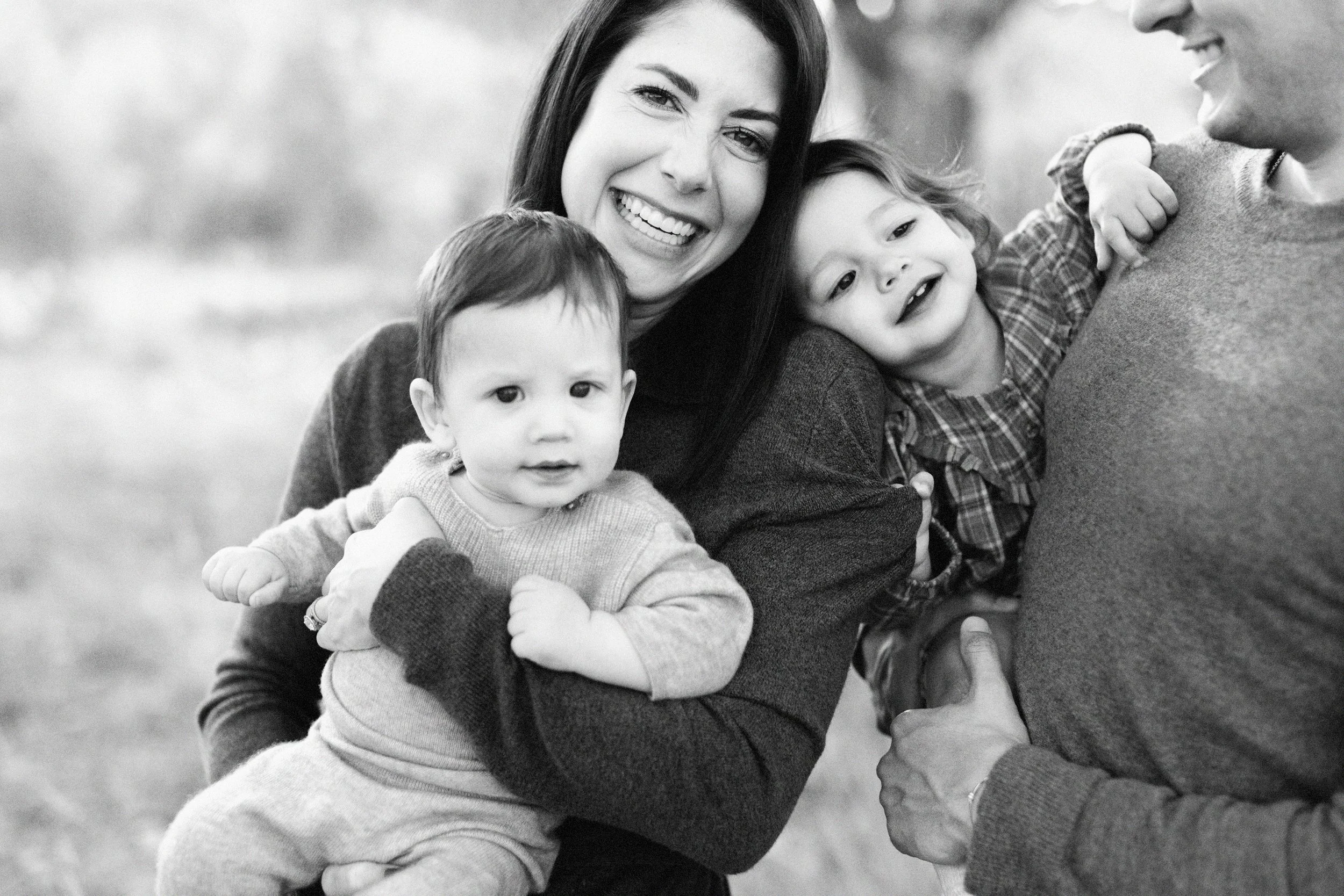 Mother cuddling her two young children in a natural black and white family portrait.