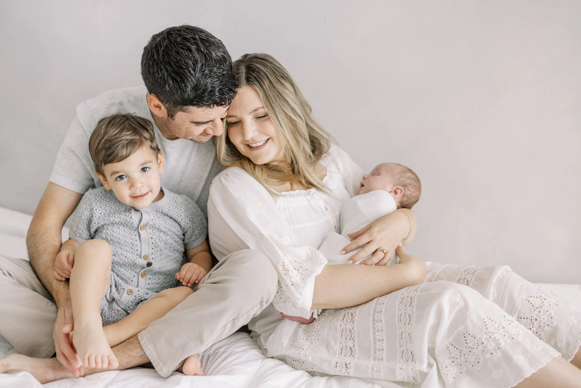 Parents smiling with their toddler while holding their newborn during a relaxed studio family portrait.