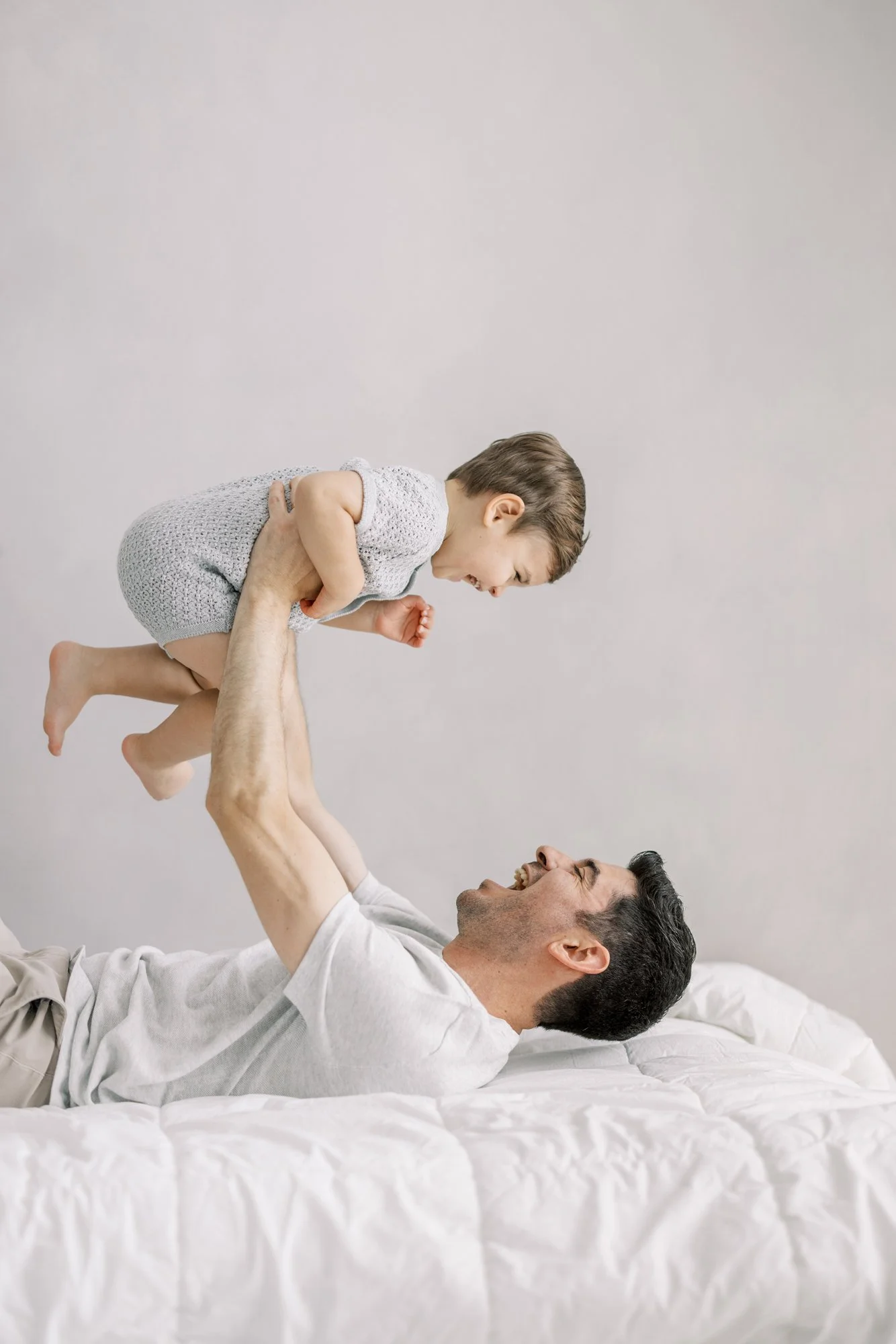 Father lifting his toddler into the air during a joyful family newborn photography session.