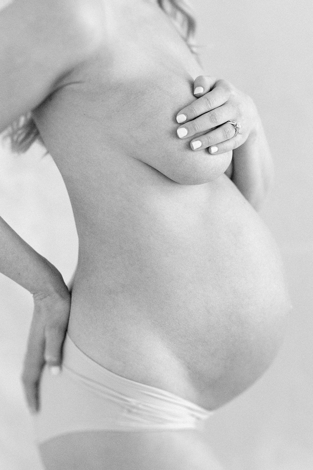 Close-up black and white portrait of a pregnant mother's baby bump with her hand gently resting across her chest.