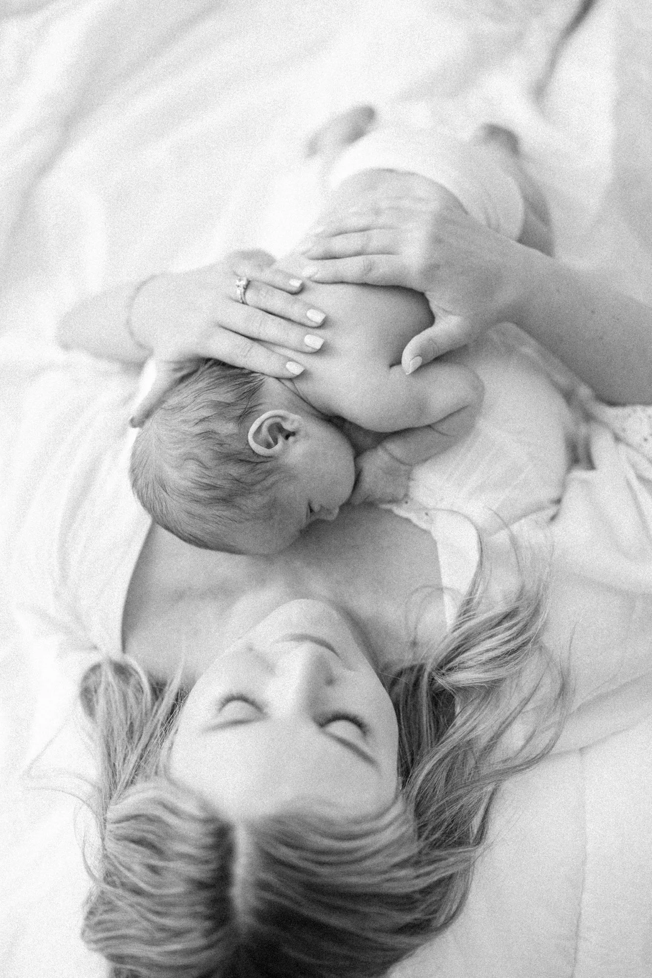 Overhead portrait of a mother holding her newborn while lying together on a bed during a newborn session.