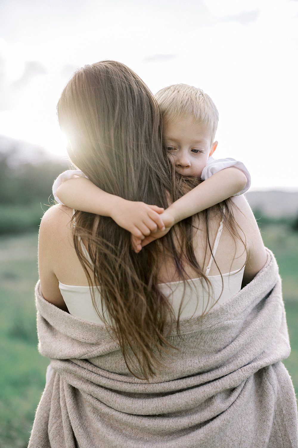 Mother holding her young son as he hugs her during an outdoor family portrait session in Denver, Colorado.