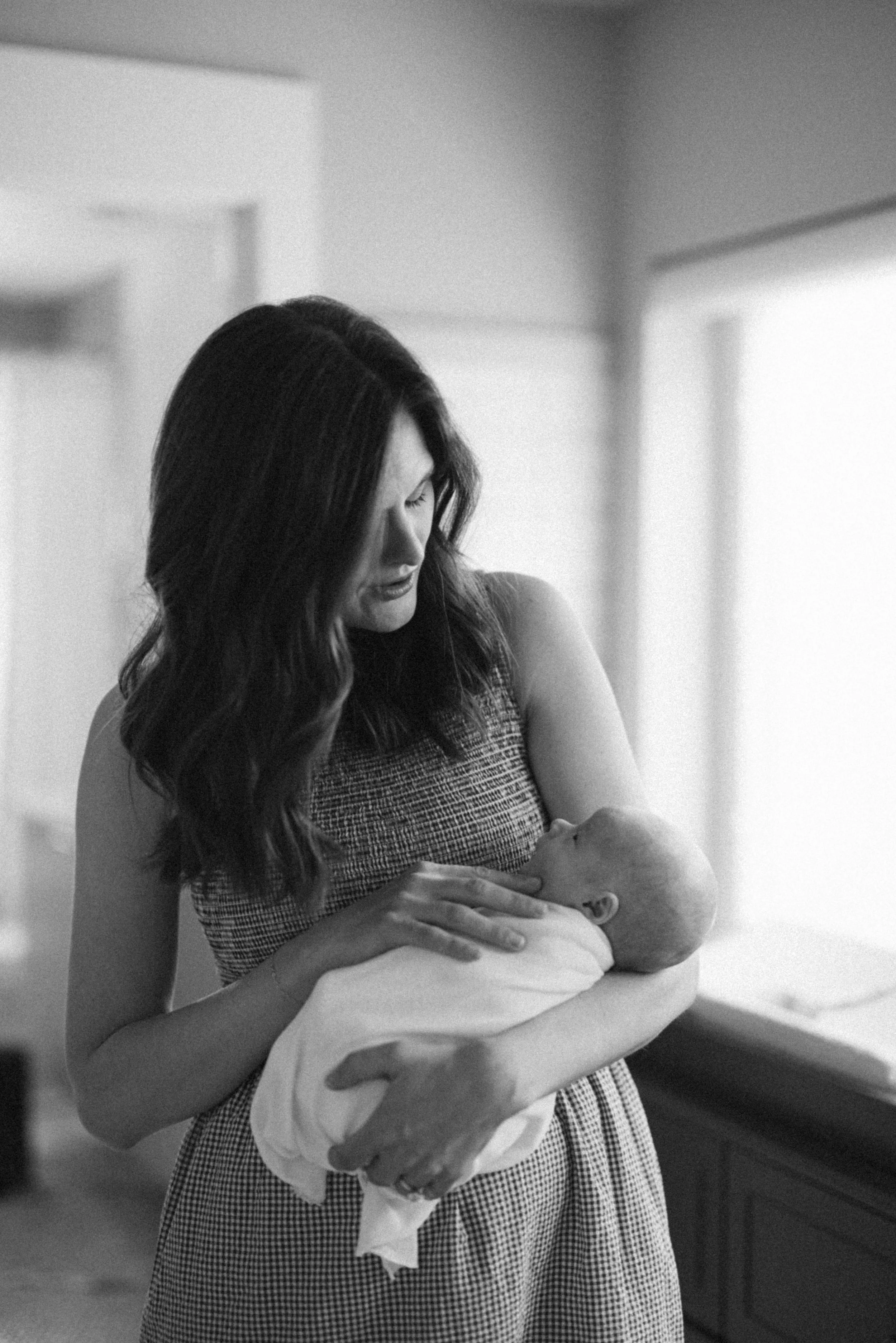 Black and white portrait of a mother holding her newborn near a window during an in-home newborn session.