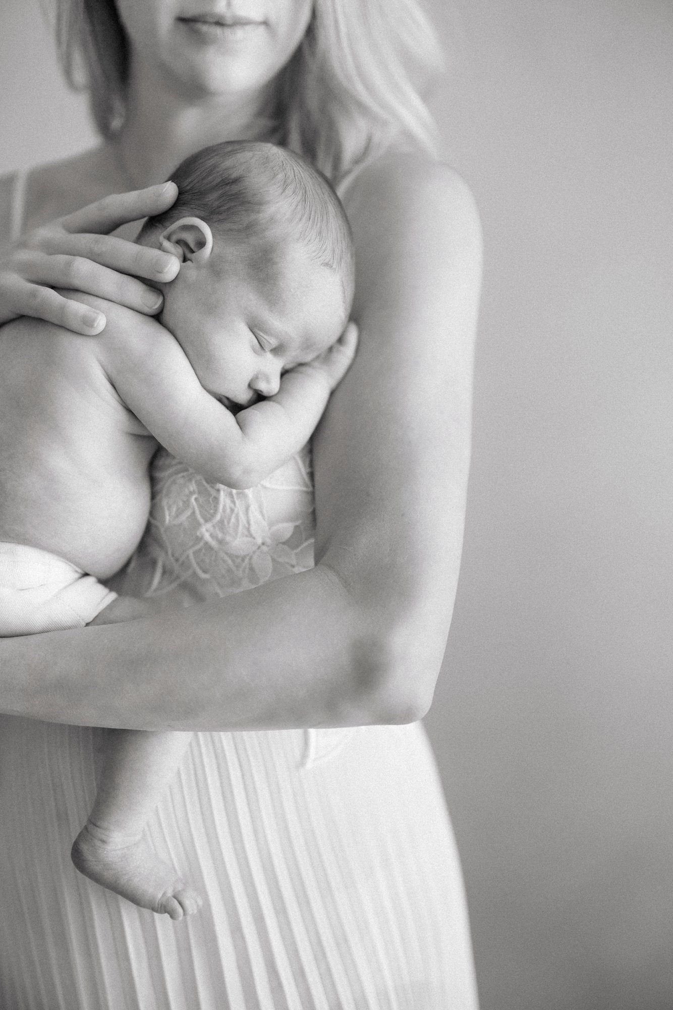 Close-up portrait of a mother gently holding her sleeping newborn during a studio newborn session.