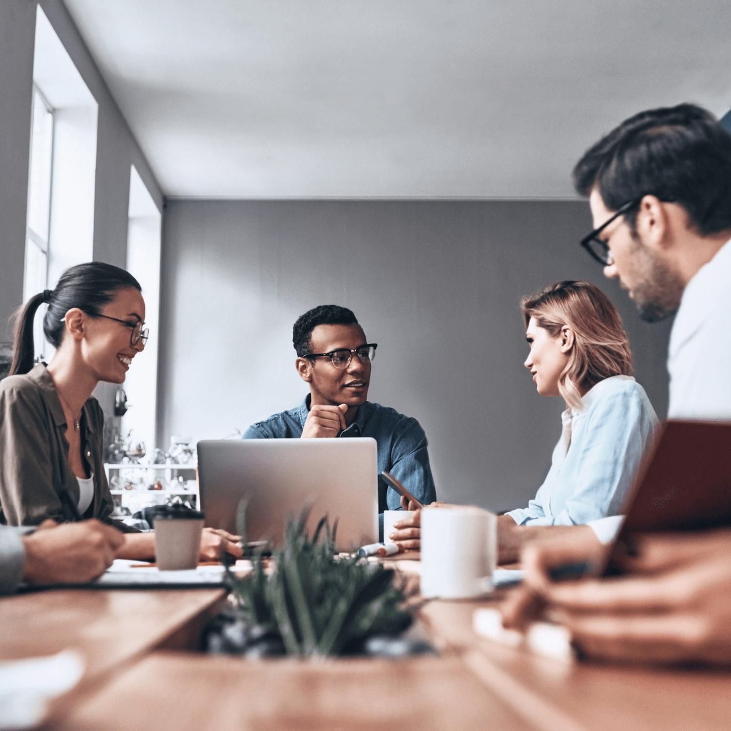 A diverse group of five people engaged in a discussion around a conference table in a modern office.