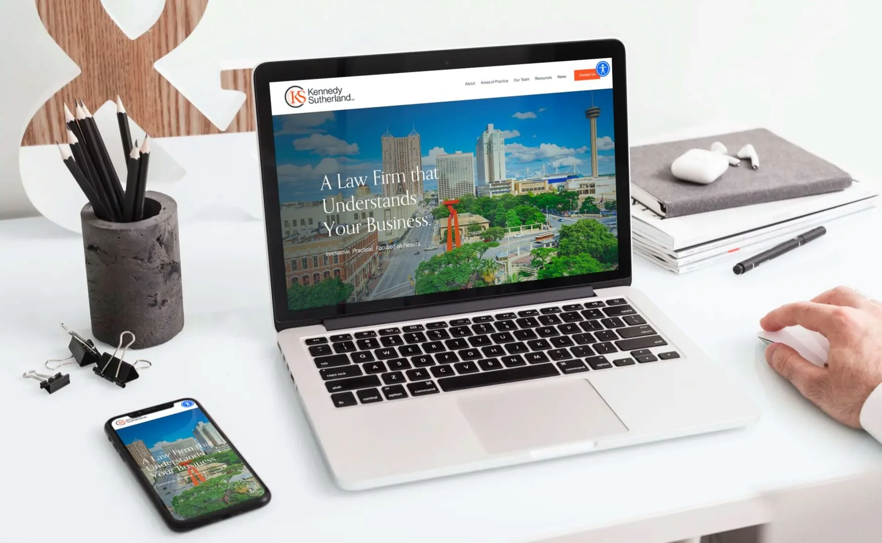 Open laptop and smartphone on a white desk displaying the same law firm website with the message "A Law Firm that Understands Your Business" and city skyscrapers in the background.