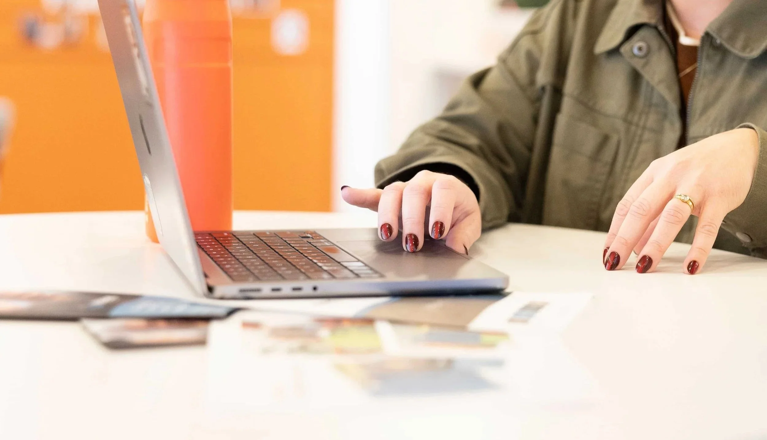 Person using a laptop sitting at a table with coffee cups and papers