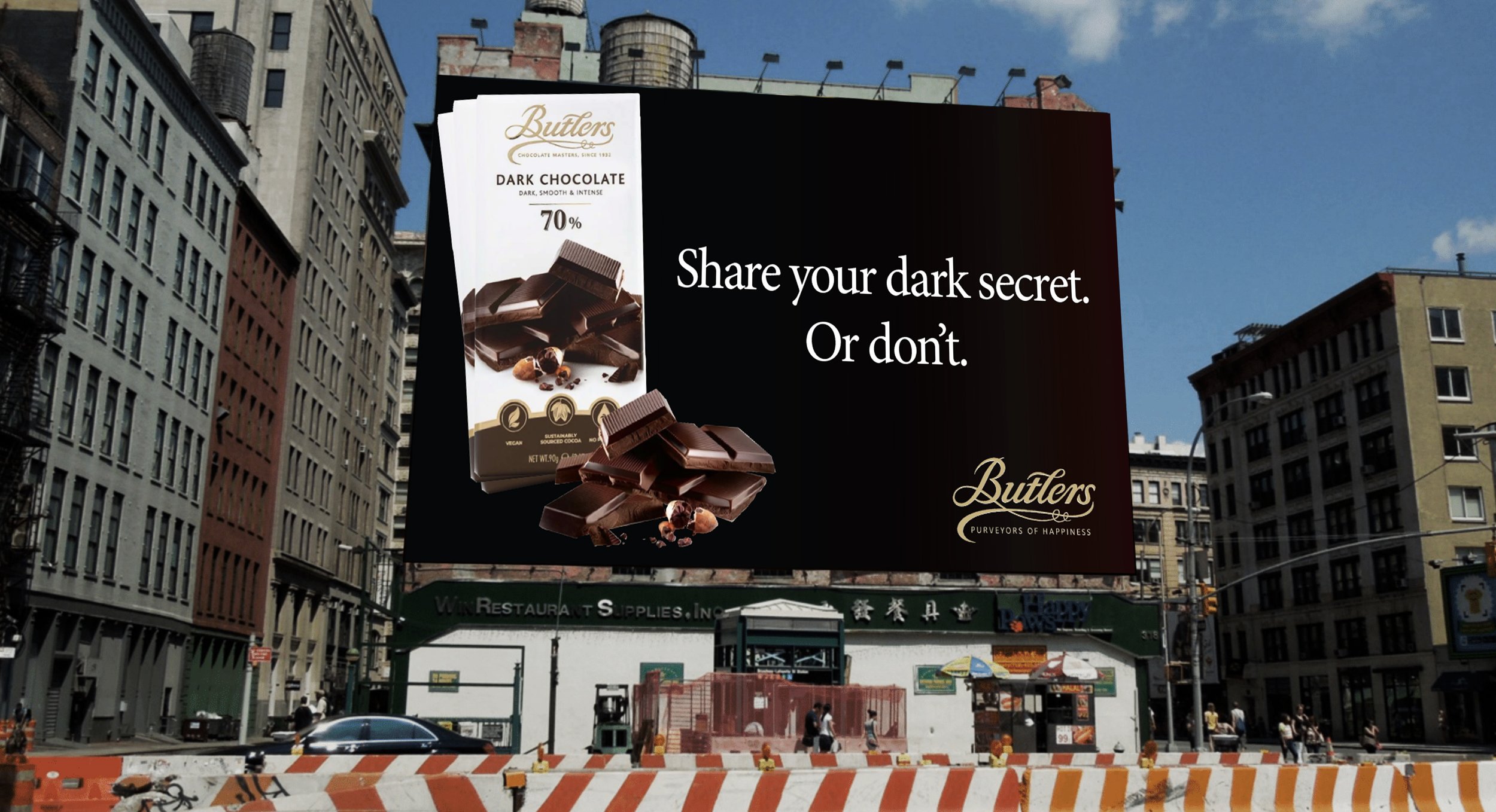 Billboard advertisement for Butlers dark chocolate, featuring a bar of dark chocolate, with the text 'Share your dark secret. Or don't.' on a city street with buildings and people.