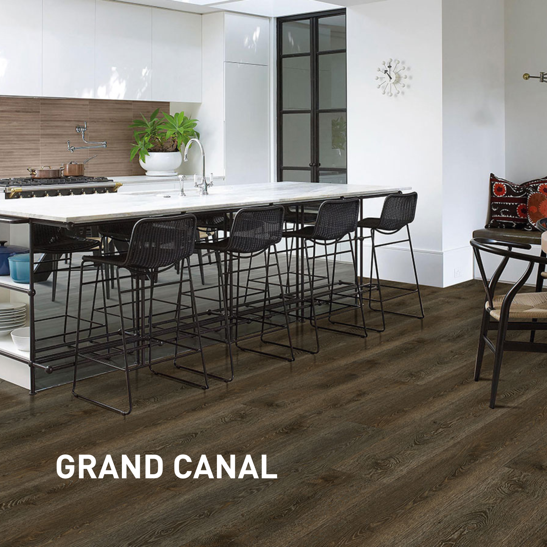 Modern kitchen with a white marble island, black bar stools, a wooden floor, and a decorative wall clock.