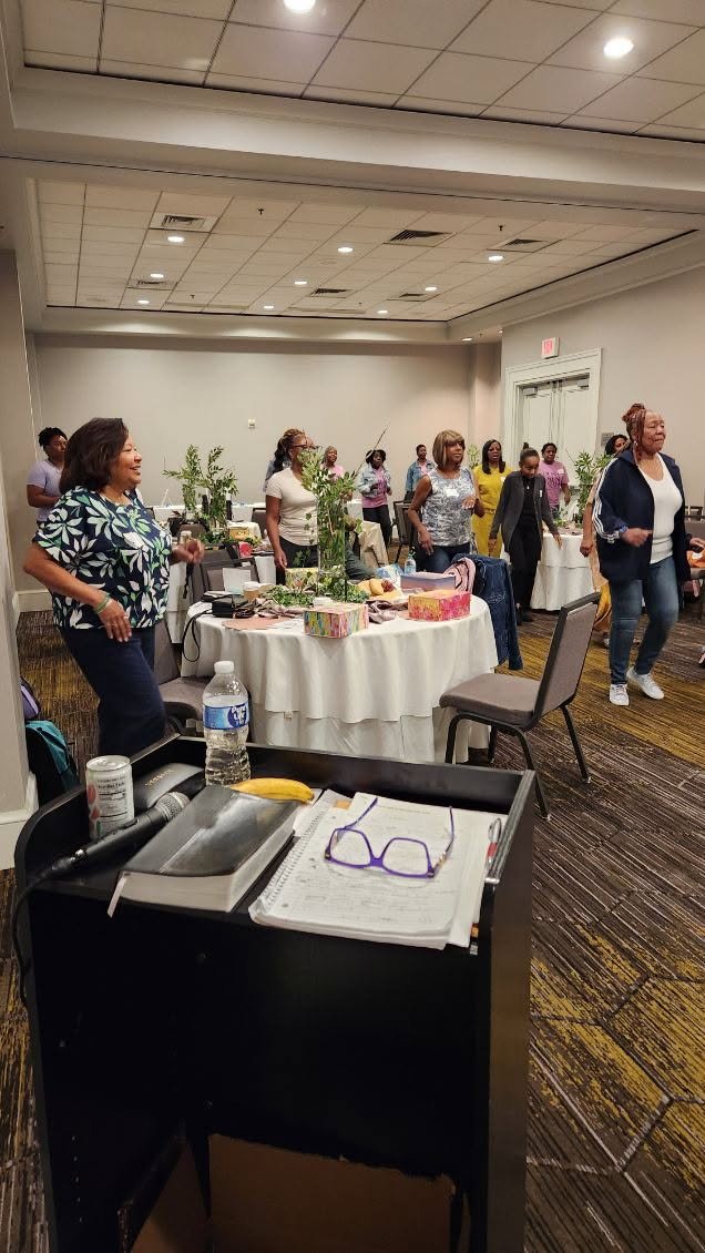 Women participating in a group activity or dance in a conference room with tables and decorations.