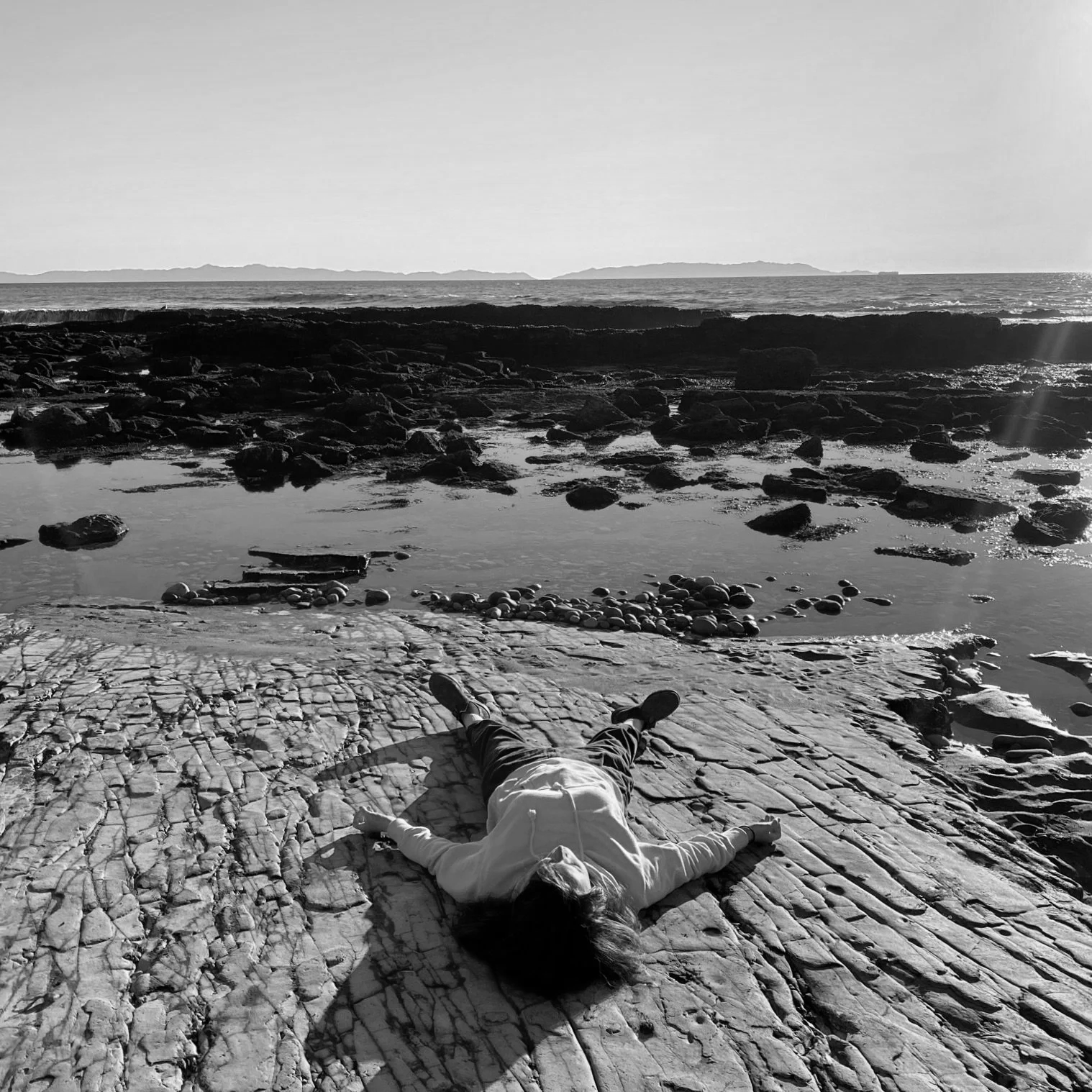 An image of savasana on a flat rock by the coast.