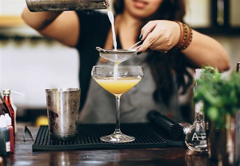 A bartender pours egg wash through a strainer into a cocktail glass.