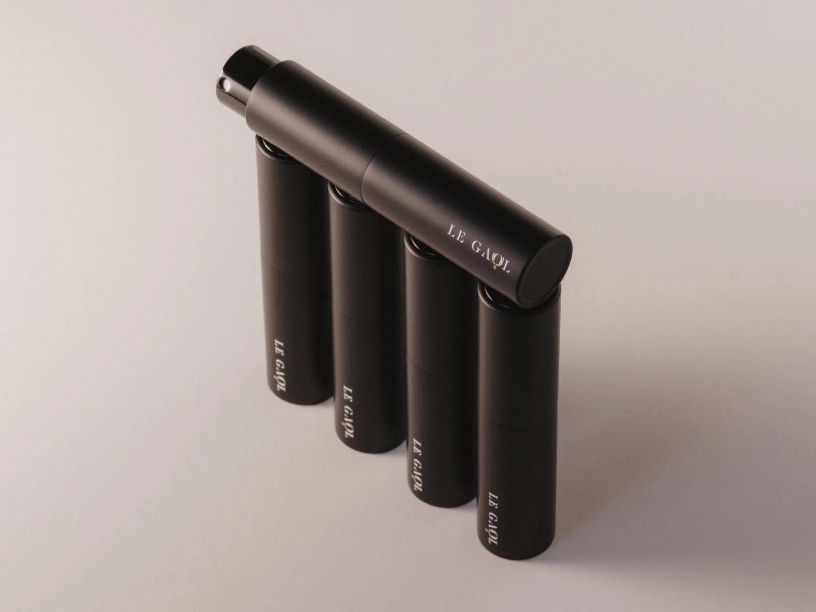 Five black Le Gaol travel fragrance sprays arranged in an architectural formation, with one spray balanced diagonally across the top.