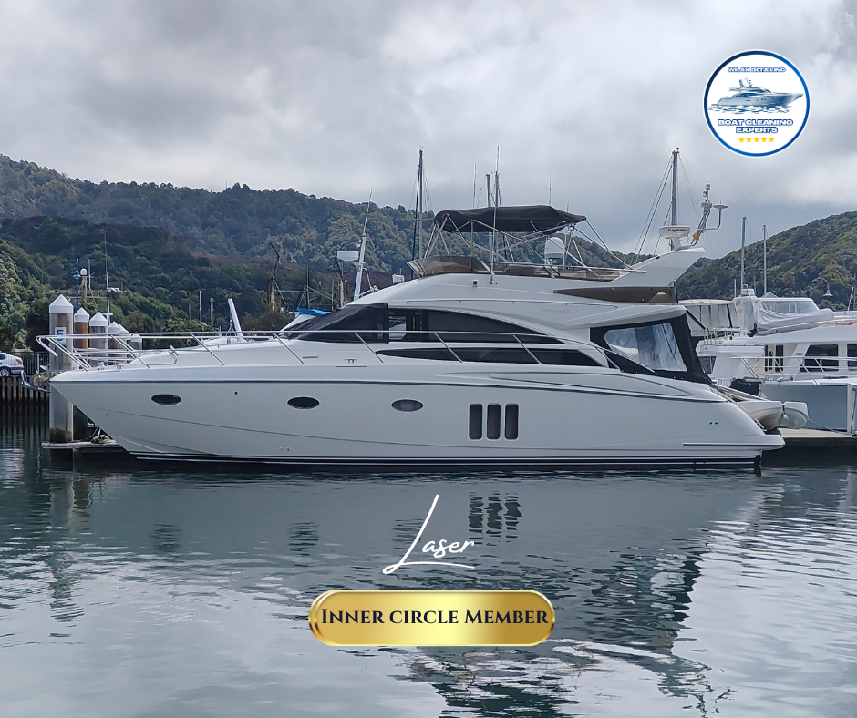 Luxury yacht docked at a marina on a sunny day, with a lush green hillside in the background.