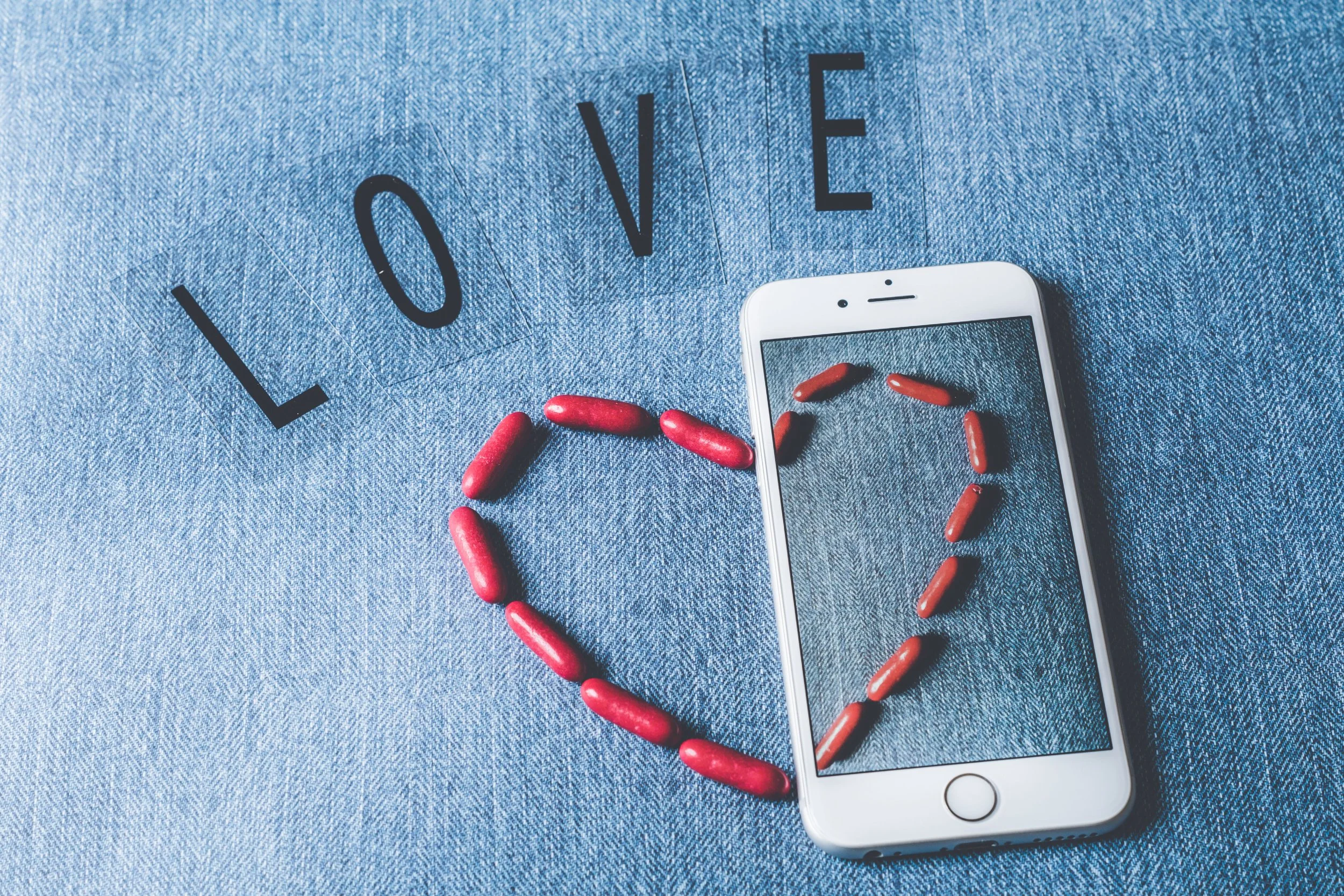 denim back ground with words 'love'written and a red love heart half on the denim half over a phone.