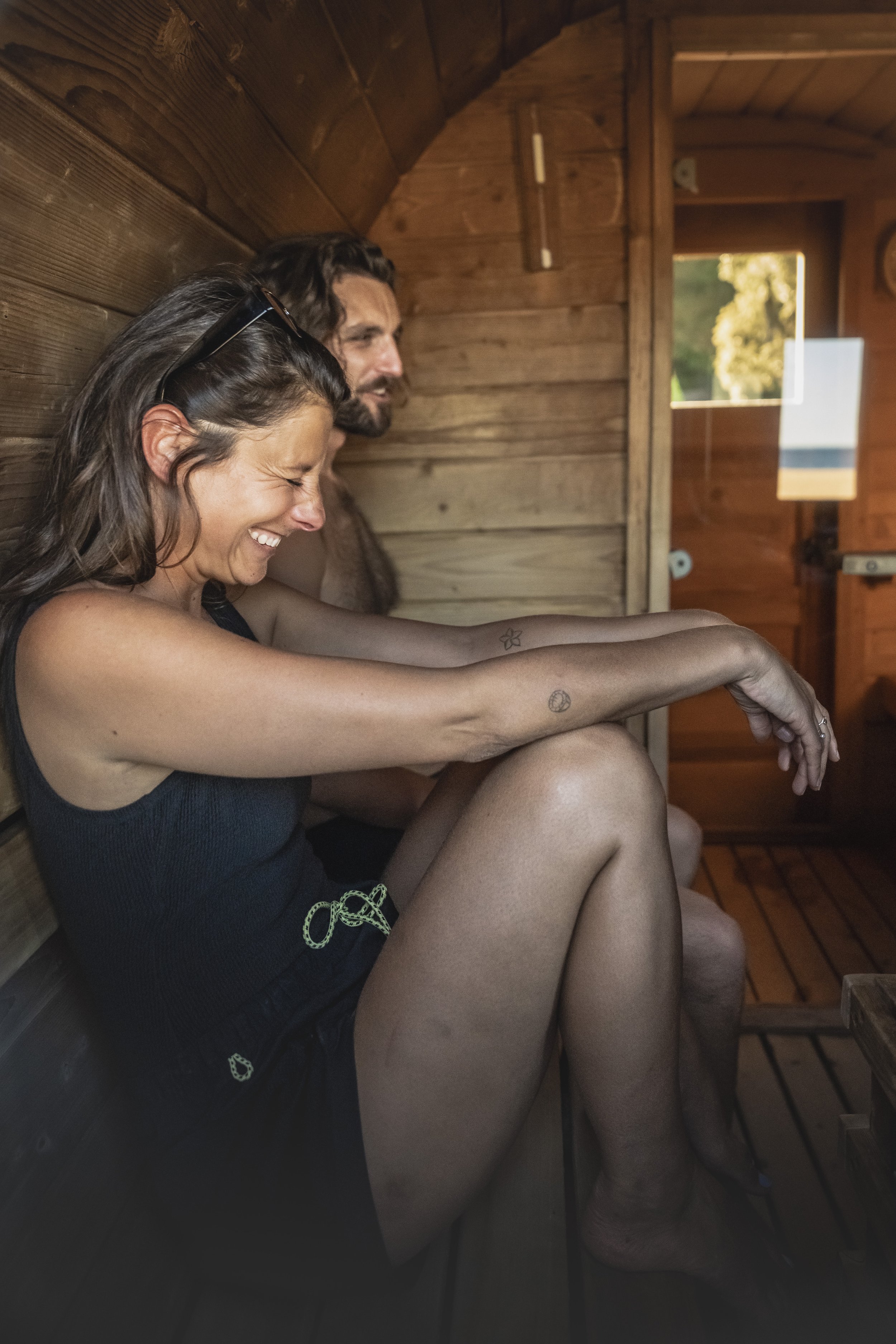 A woman laughing inside a wooden sauna with a man behind her.