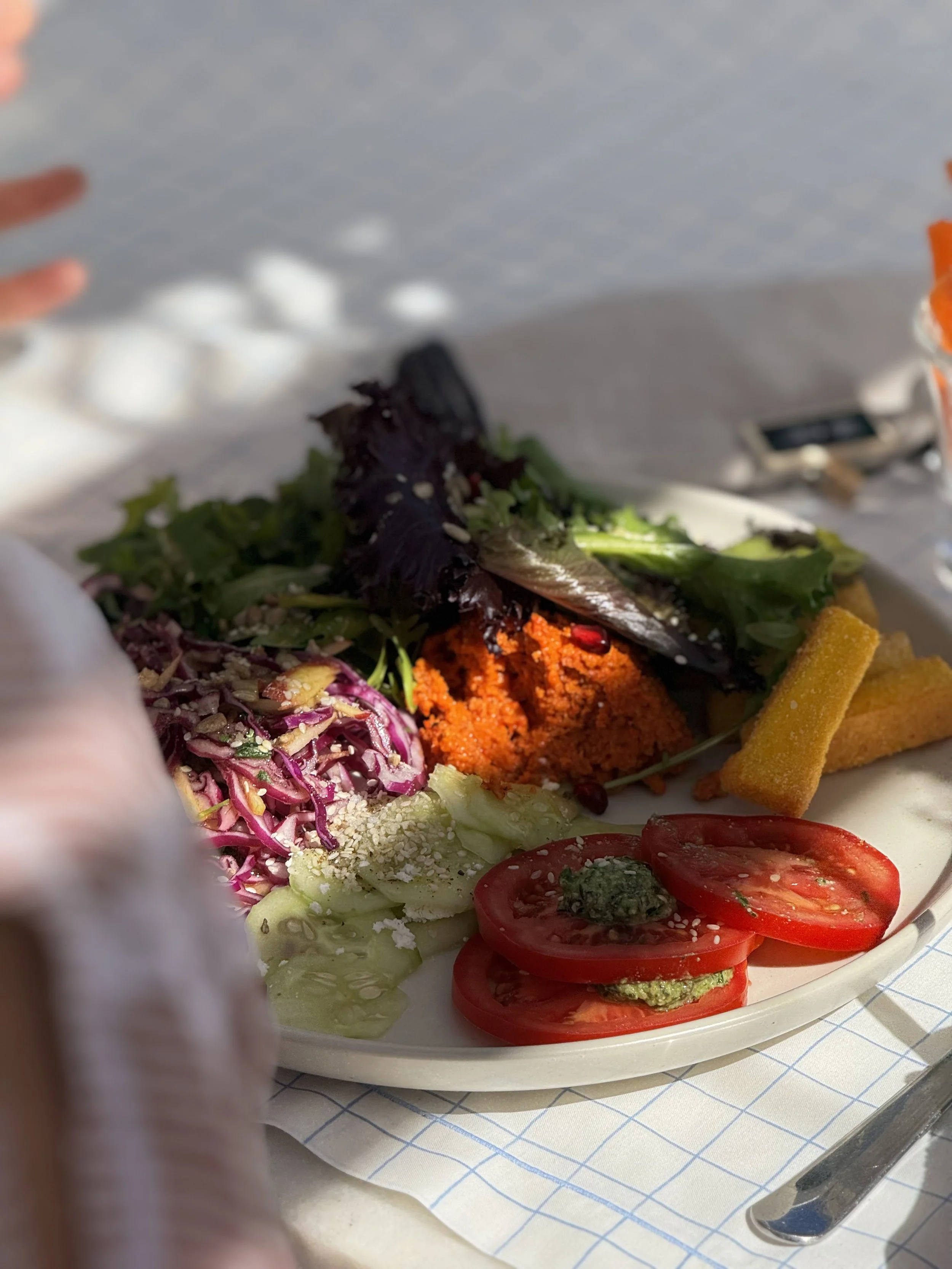 A plate of salad with cherry tomatoes, lettuce, purple cabbage, and a scoop of orange-colored side dish, possibly hummus or dip, garnished with herbs and sunflower seeds. yummy yoga retreat food