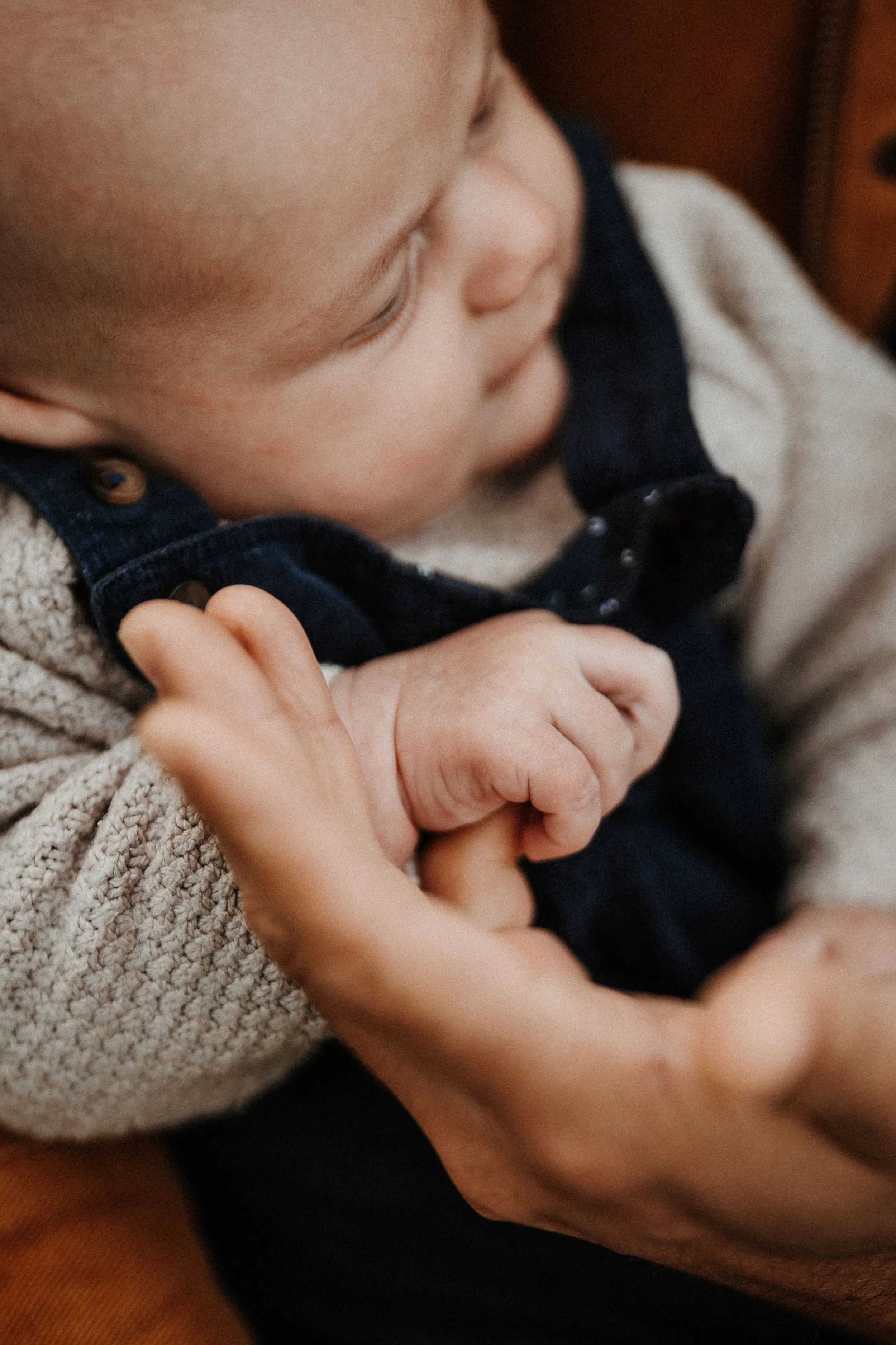 Détail des mains d’un bébé tenant le doigt de son parent lors d’une séance photo famille naturelle
