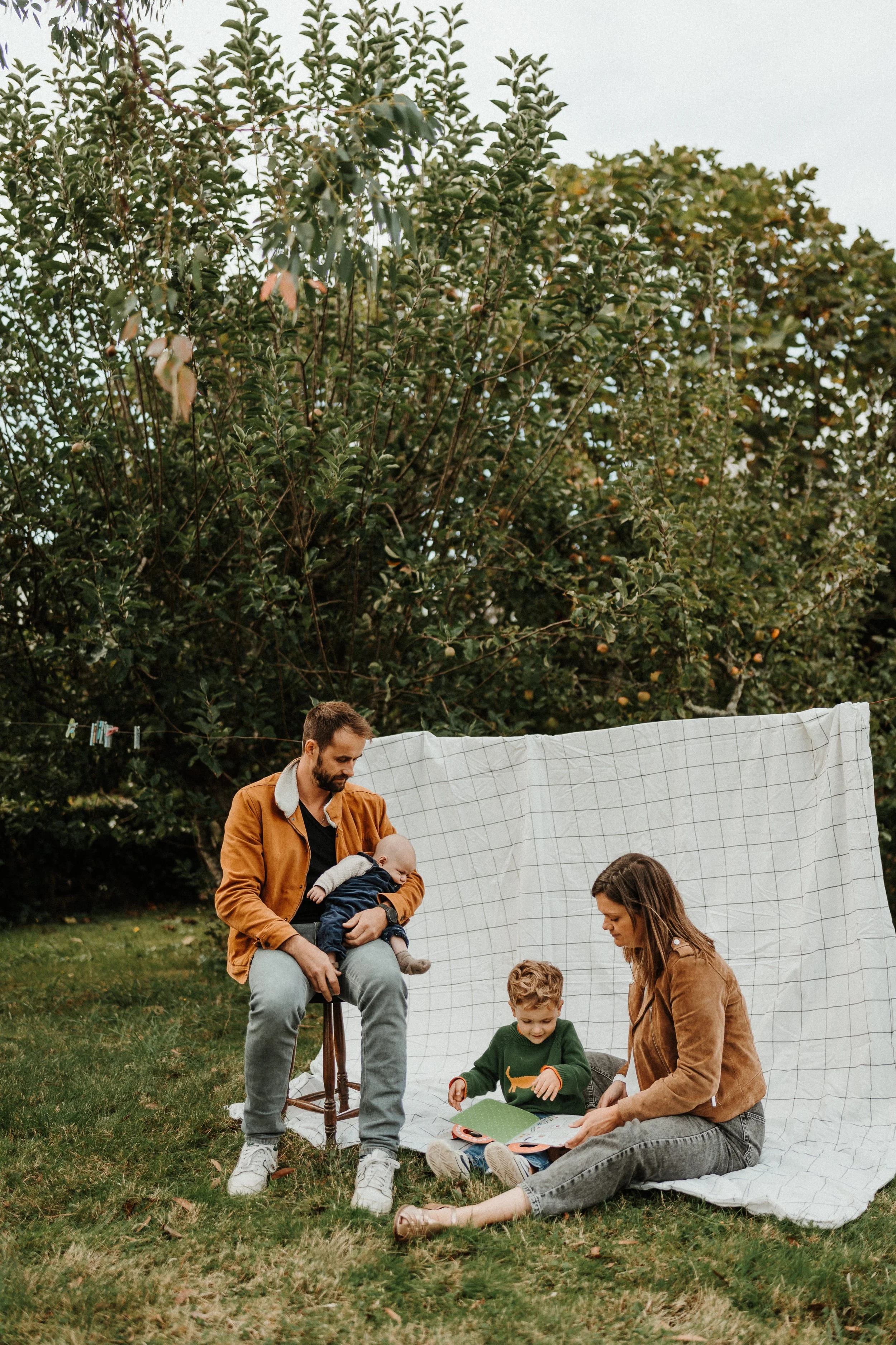 Séance photo famille lifestyle dans un jardin, parents et enfants installés sur une couverture