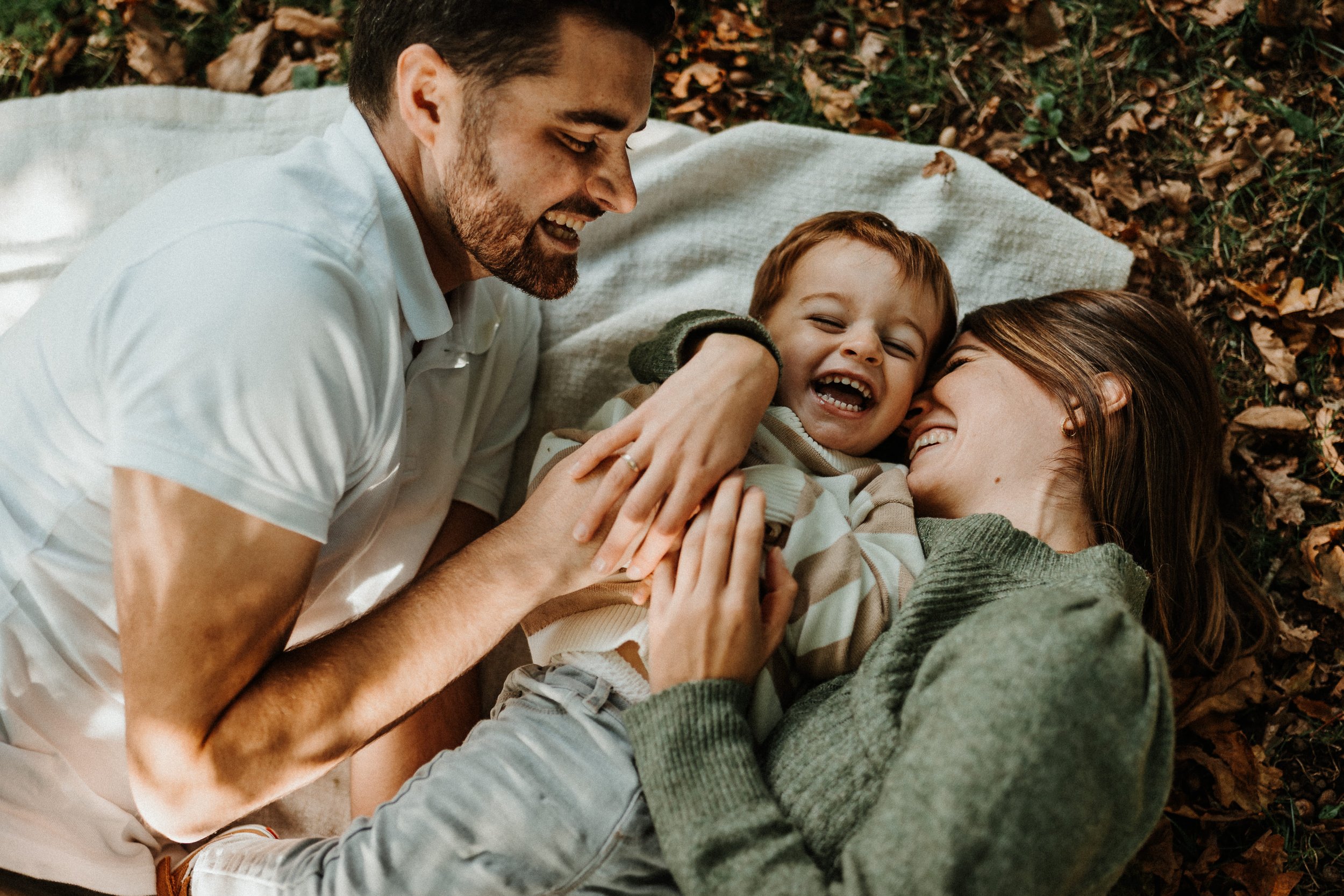Séance photo famille lifestyle, parents et enfant qui rient ensemble en extérieur en Bretagne