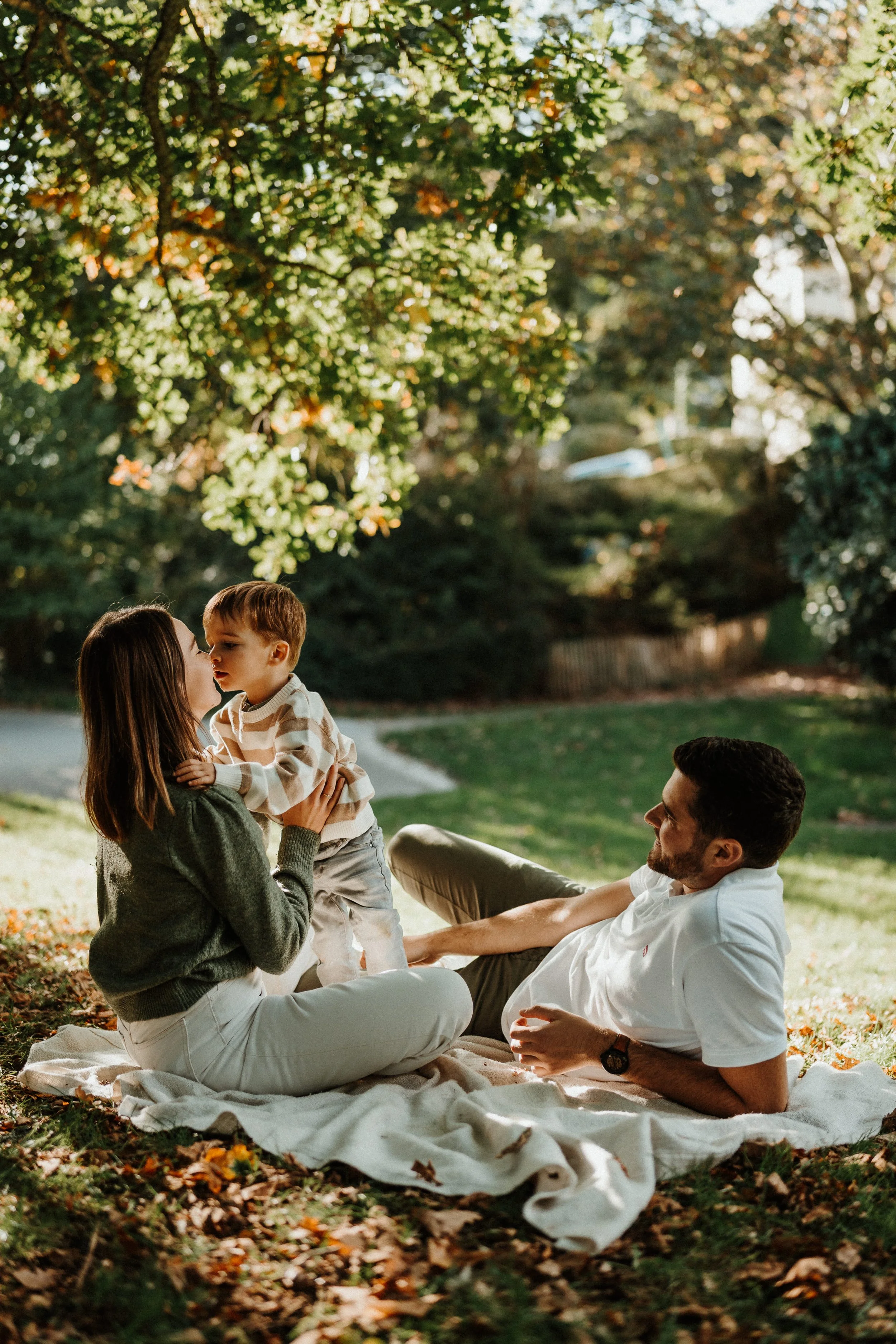Photo de famille en extérieur, parents et enfant réunis sur un plaid lors d’une séance lifestyle en Bretagne