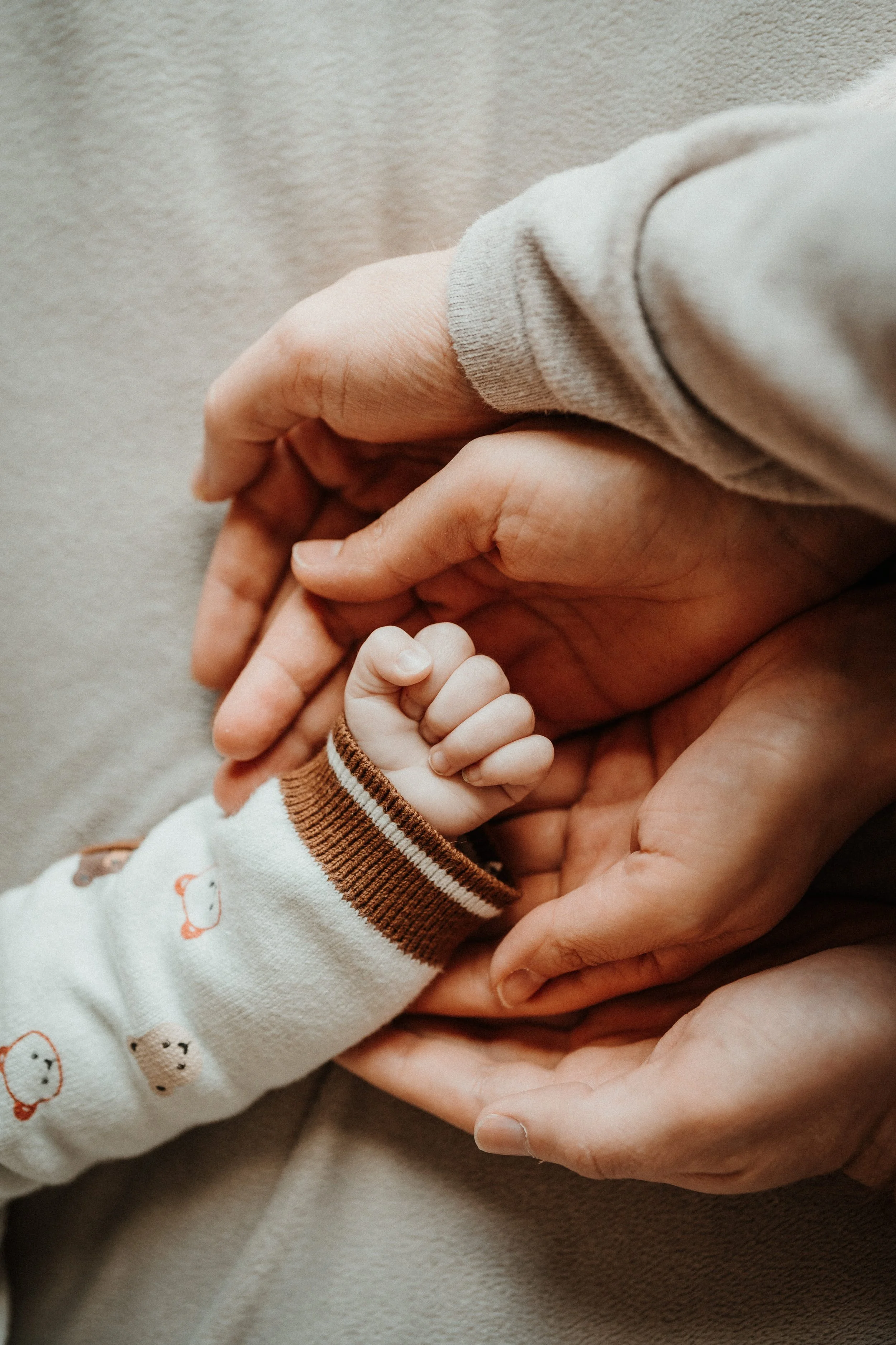 Mains des parents entourant la main de leur nouveau-né pendant une séance photo naissance à domicile