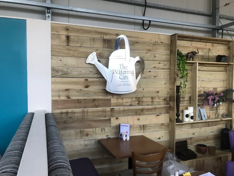 Silver watering can sign mounted on a wood style wall