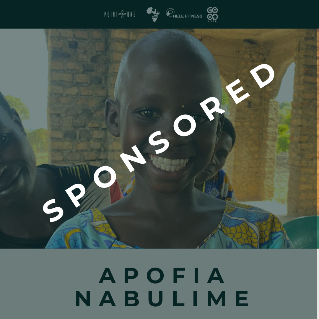 Smiling young girl with short hair, wearing a colorful patterned dress, standing indoors with a stone wall and arched window in the background, part of a group of people with the word "SPONSORED" across the photo diagonally. 