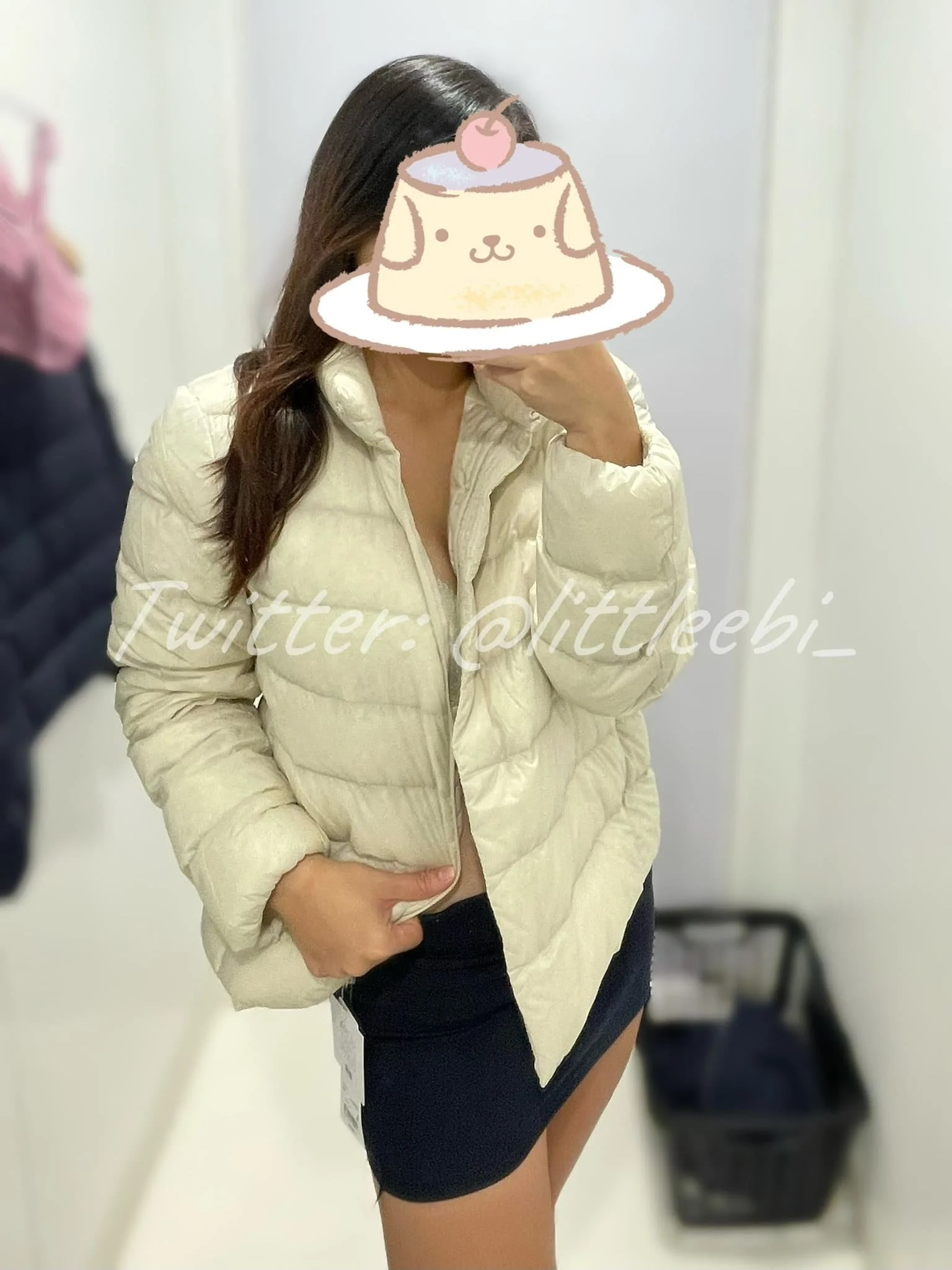 Person in a cream-colored puffer jacket and black skirt taking a mirror selfie; face covered with a cute sticker of a dessert with a face, cherry, and whipped cream.