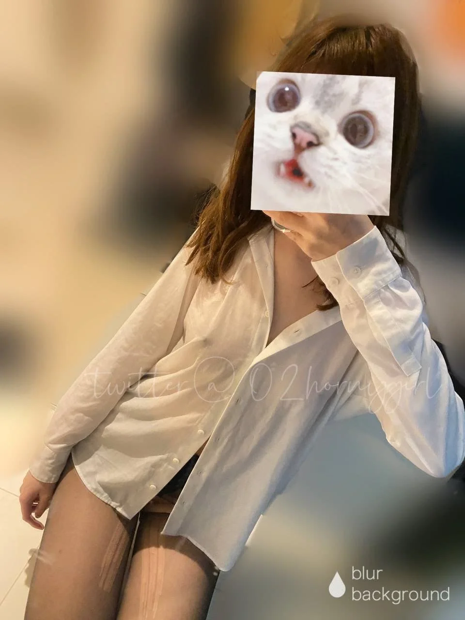 Person taking a mirror selfie, wearing a white shirt and sheer tights, with their face covered by a meme of a cat with large eyes and a surprised expression.