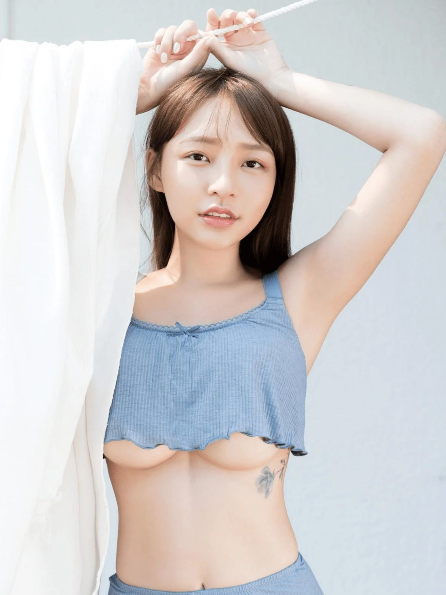 Person in blue outfit posing outdoors, holding a rope above their head.