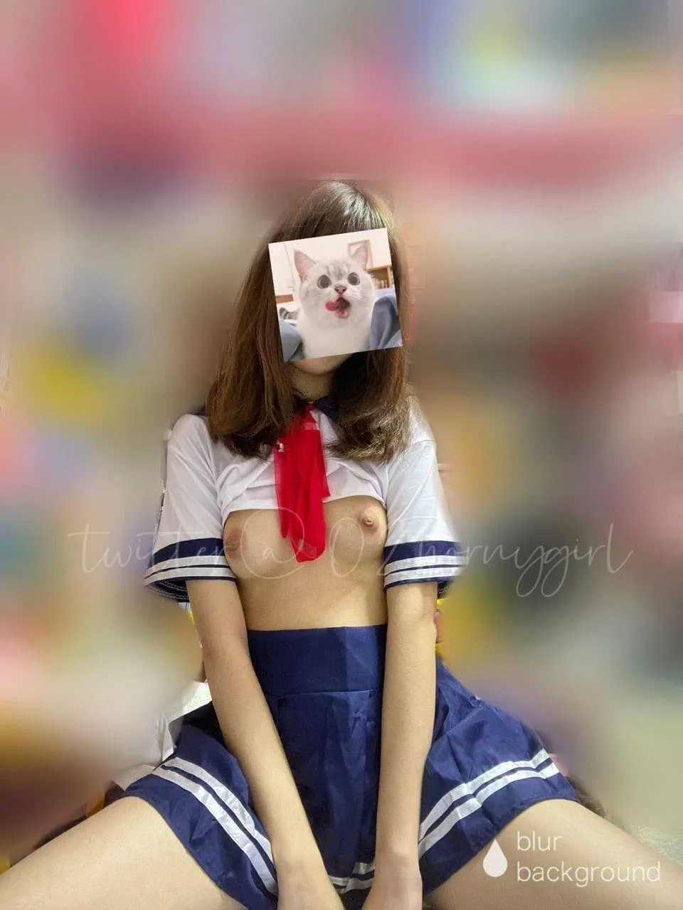 Person wearing a schoolgirl outfit with a shirt and skirt, sitting on the floor in a colorful blurred background. Their face is covered with a meme of a surprised cat with an open mouth.