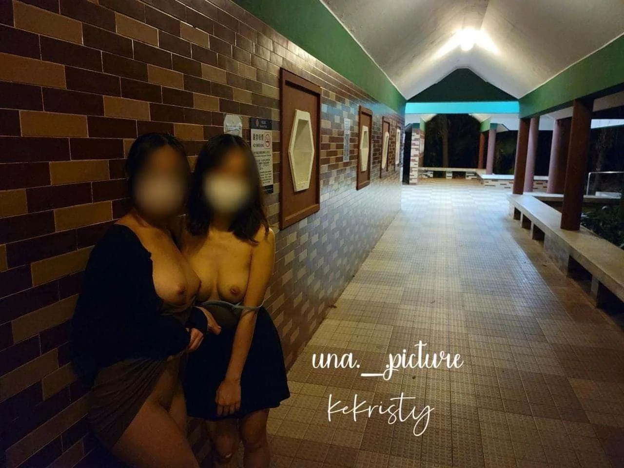 Two women with blurred faces standing on a covered walkway at night, leaning against a brick wall, with the woman on the left holding a small purse and the woman on the right wearing a black skirt and beige top.