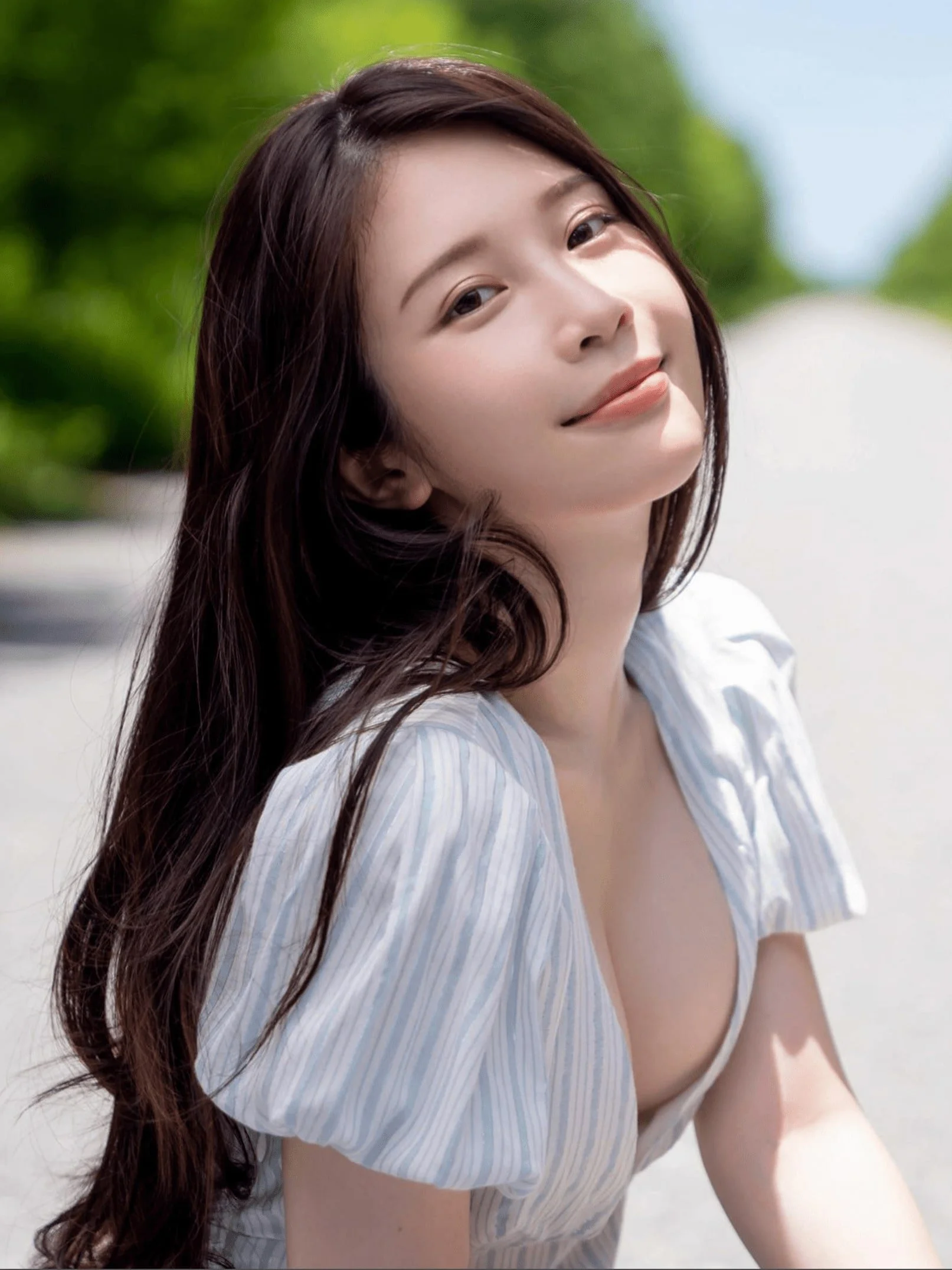Woman with long hair in a light blue striped top, smiling outdoors.