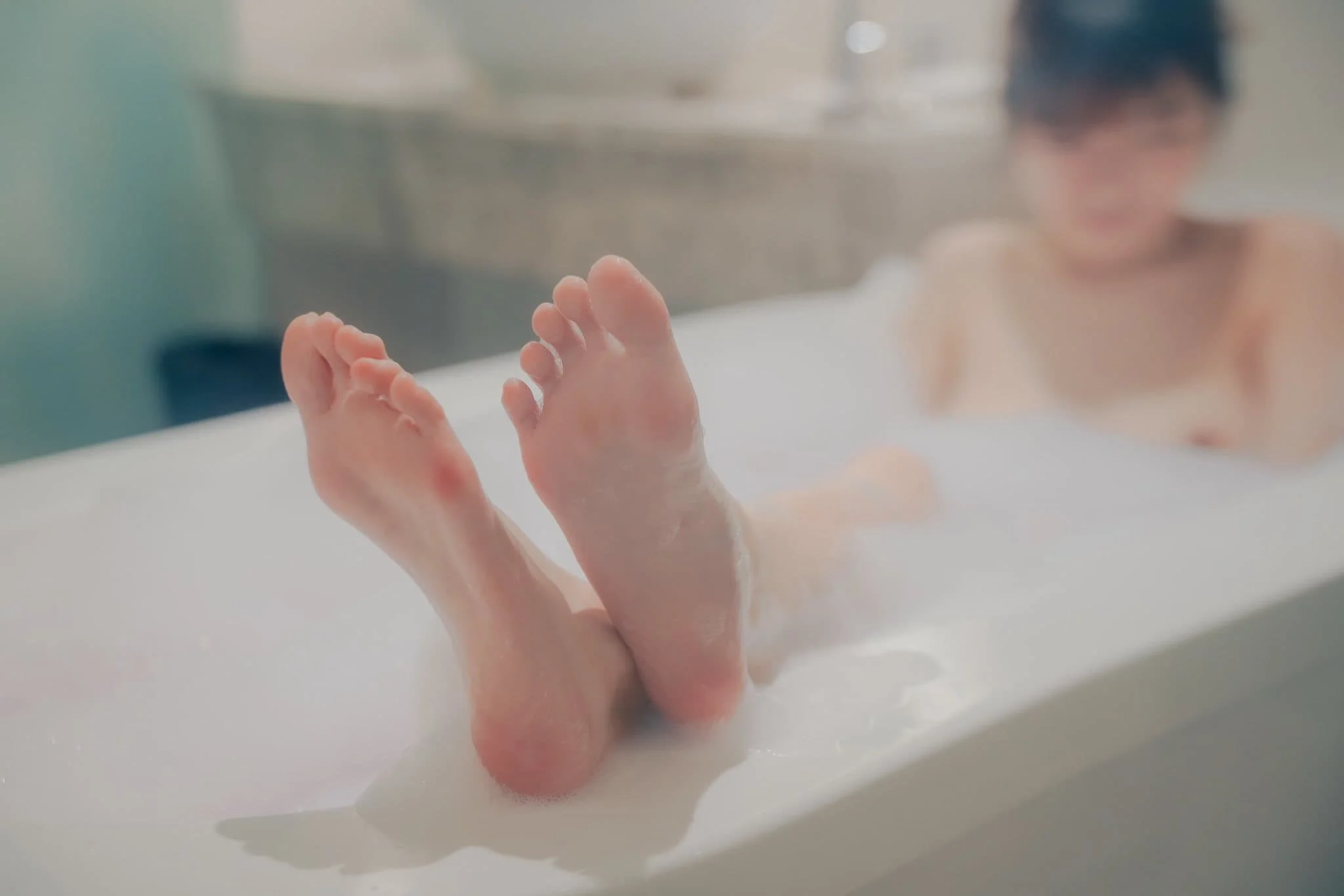 Child relaxing in a bubble-filled bathtub, feet resting on the edge, with a blurred background of a bathroom setting.