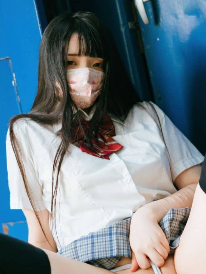 A person wearing a school uniform and a patterned face mask, sitting down.