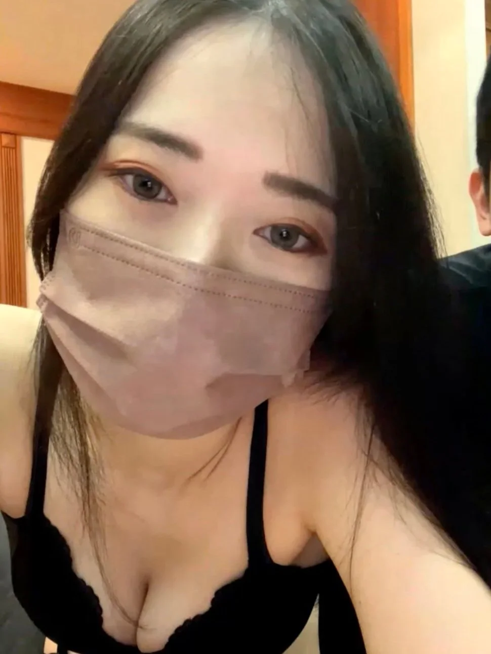 Woman with long dark hair wearing a face mask and a black top, looking at the camera.