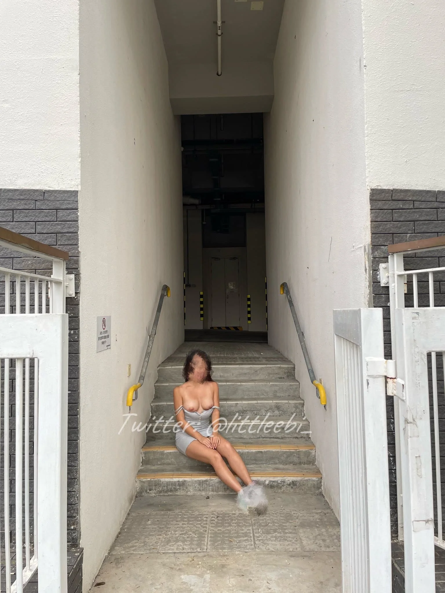A woman sitting on concrete stairs with her feet in a fountain, in an entryway with white and black brick walls and a dark corridor in the background.