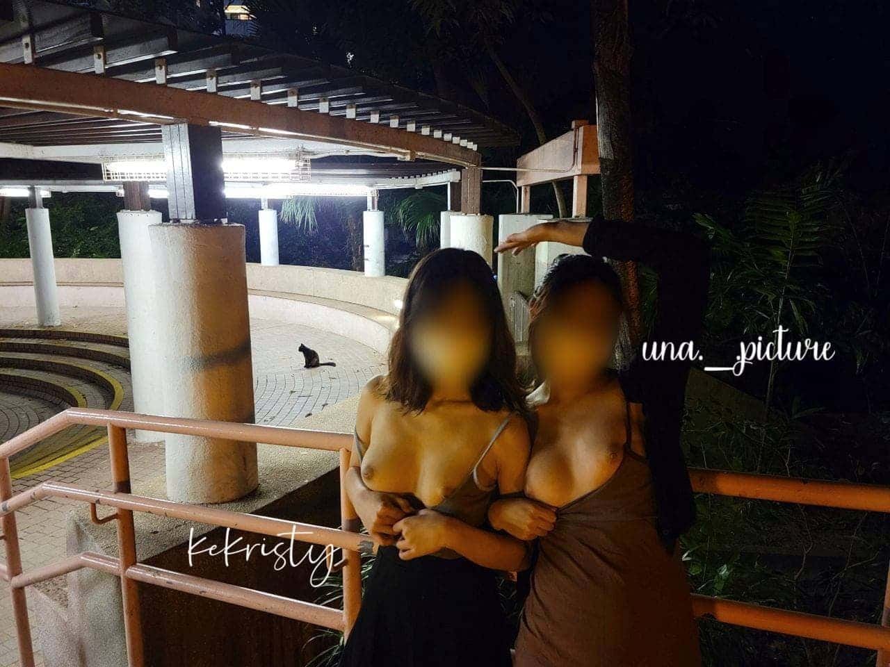 Two women with blurred faces posing together on a balcony at night, with one hand on each other's shoulders, while a person with a blurred face soutains a hand above them. In the background, a black cat sits on the ground near white columns and a cur