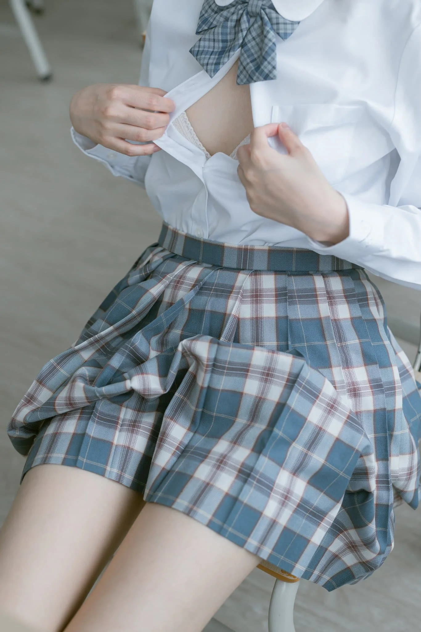 A person wearing a school uniform raising their white shirt to reveal a white lace bra.