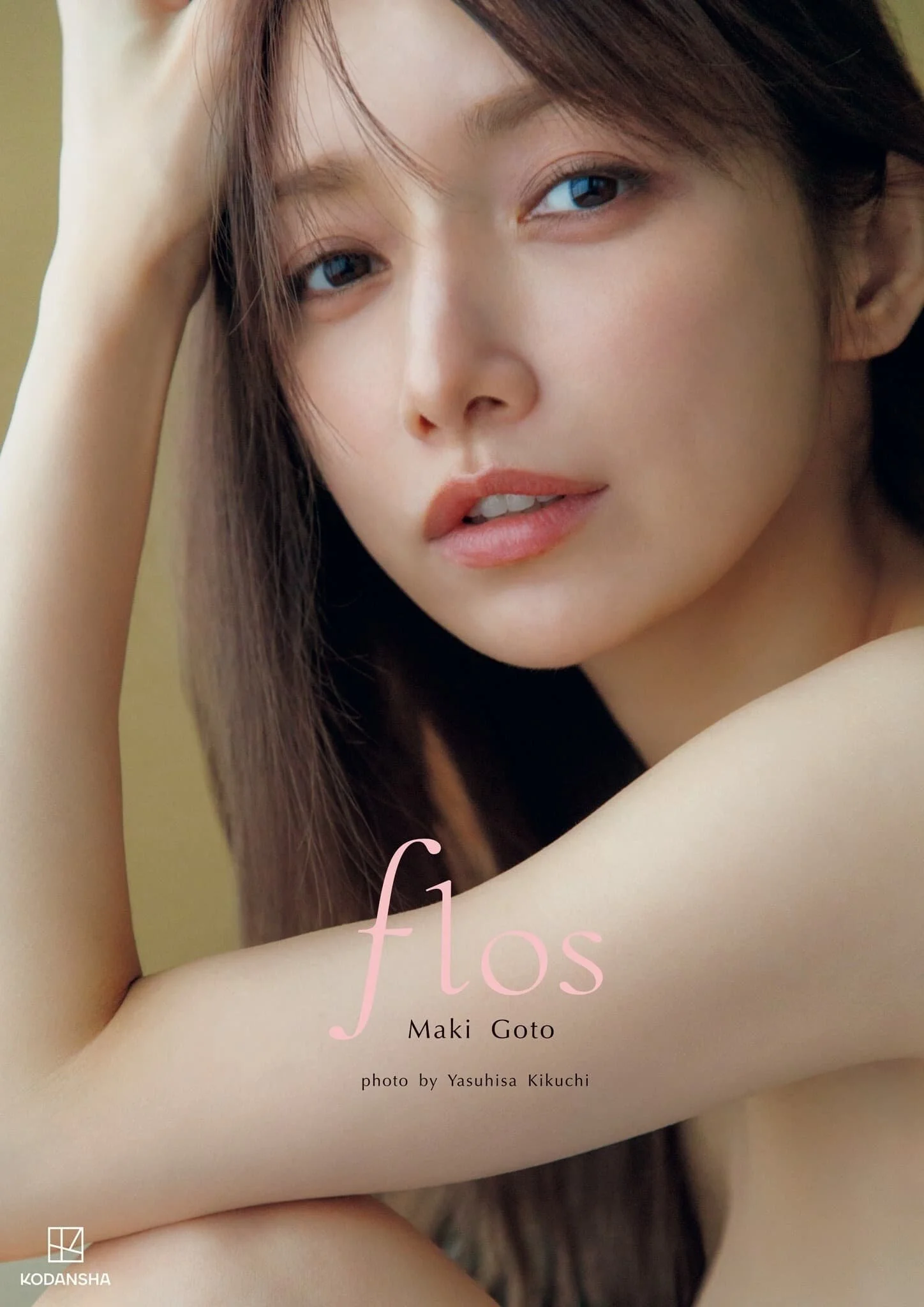Close-up of a young woman with long brown hair, looking directly at the camera with a relaxed expression, against a soft background. The image appears to be the cover of a fashion or photography book titled 'flos' by Maki Goto, with photography by Ya