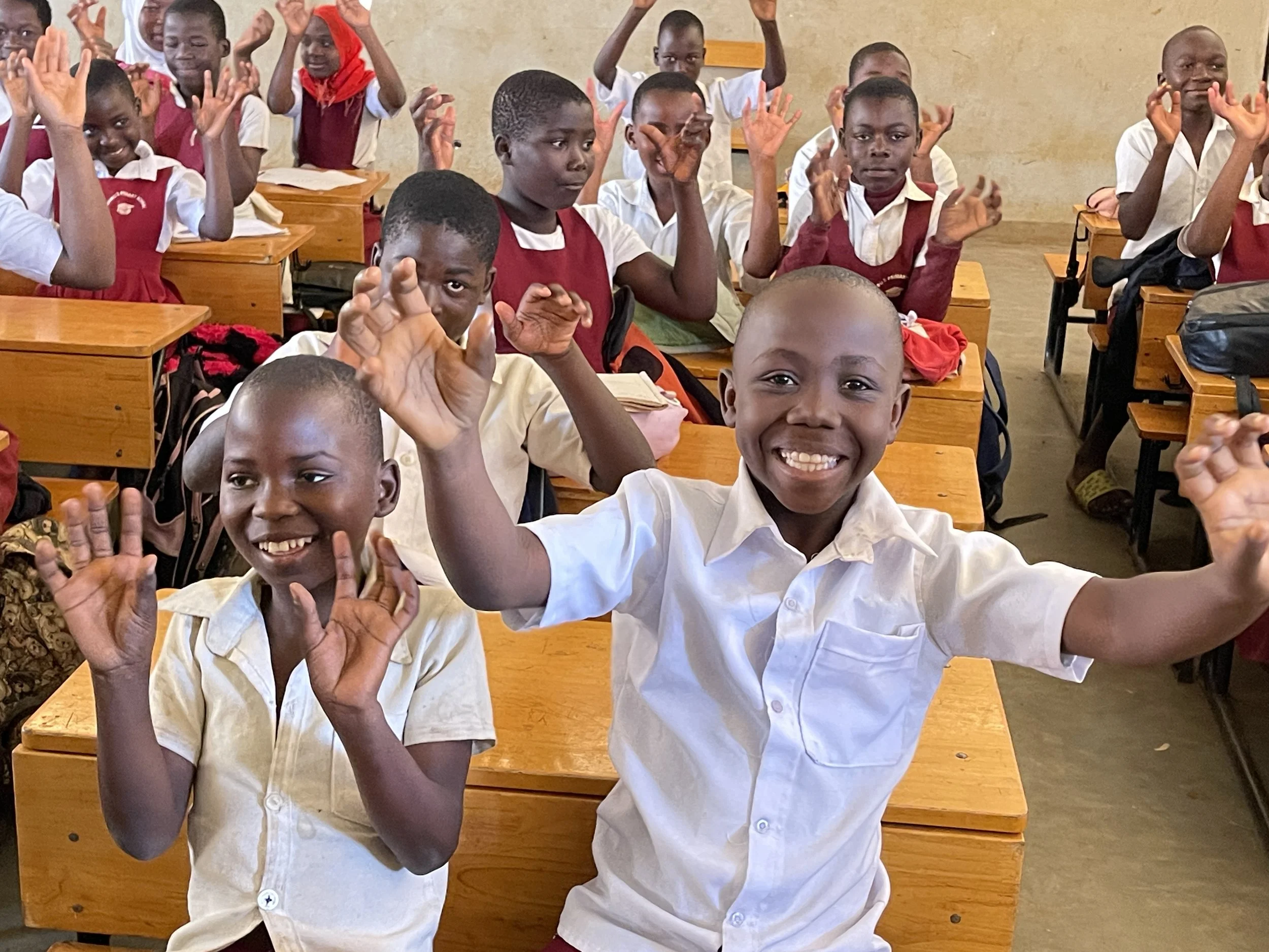 Children in school uniform waving and smiling at a visitor from E3