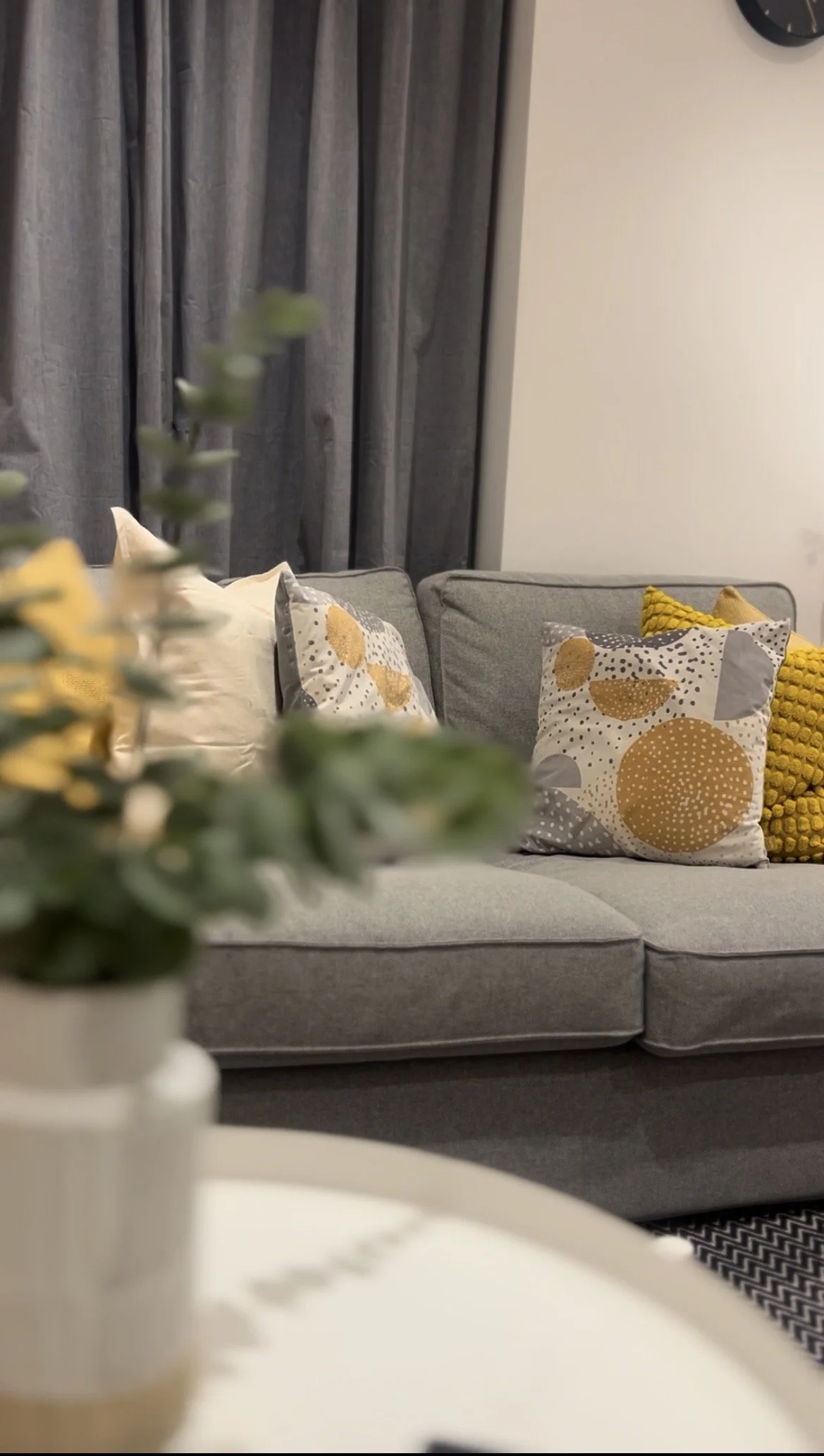 Living room with a gray sofa decorated with patterned cushions and dark curtains behind.